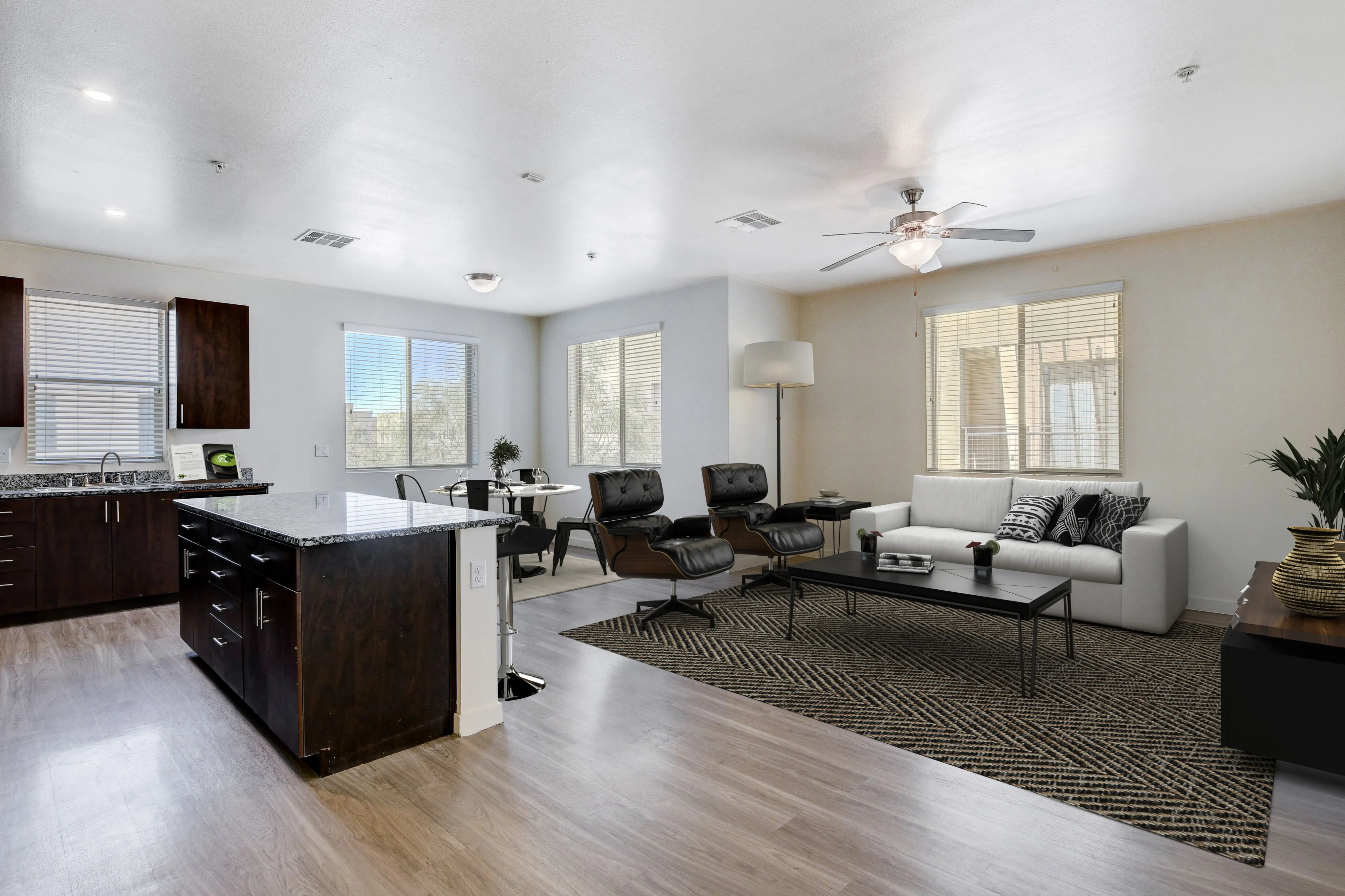 Modern open-concept living area with wood flooring, stylish kitchen island, and cozy seating area, bathed in natural light.