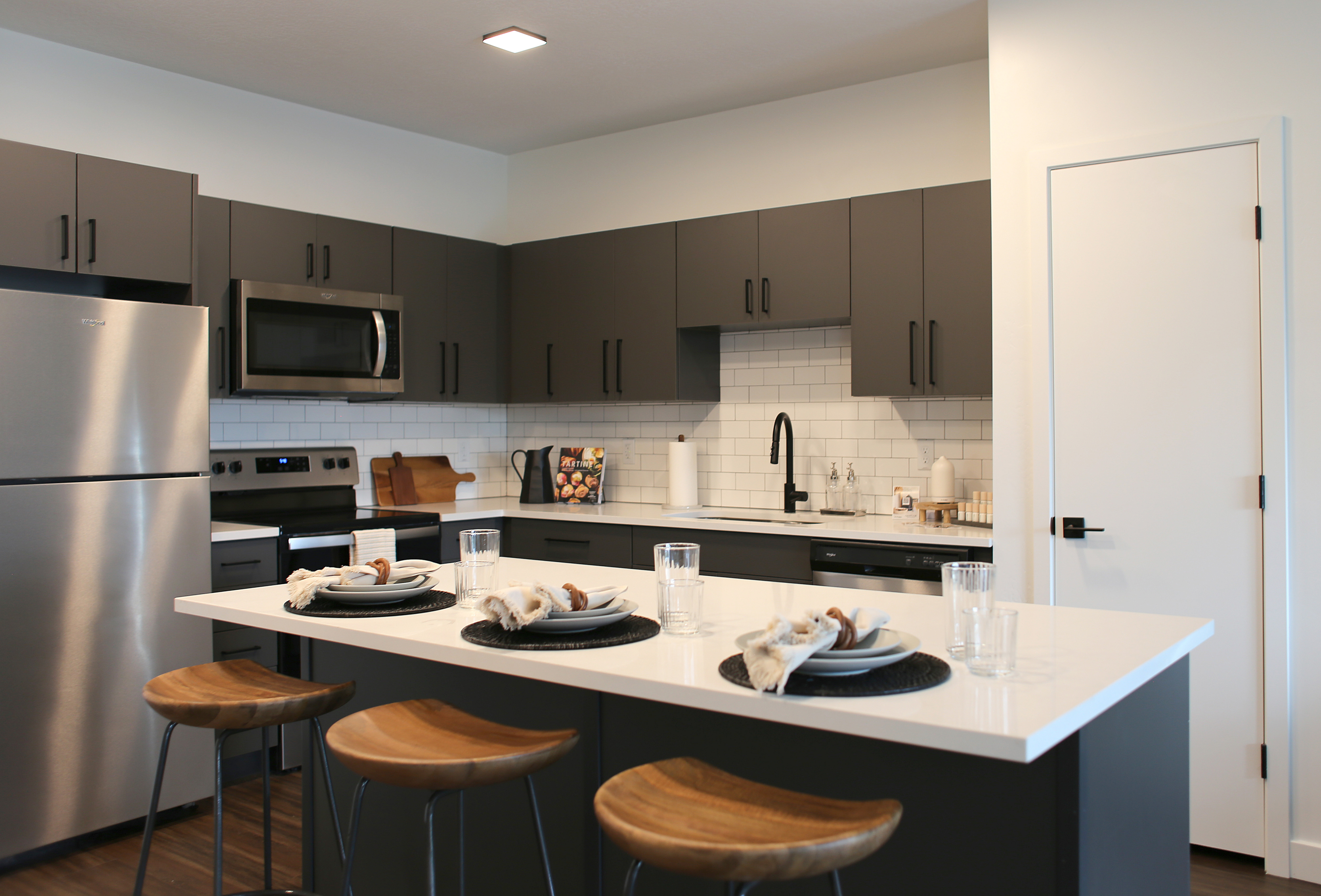 Modern kitchen with sleek gray cabinets, stainless steel appliances, and a stylish island seating area featuring wooden stools.
