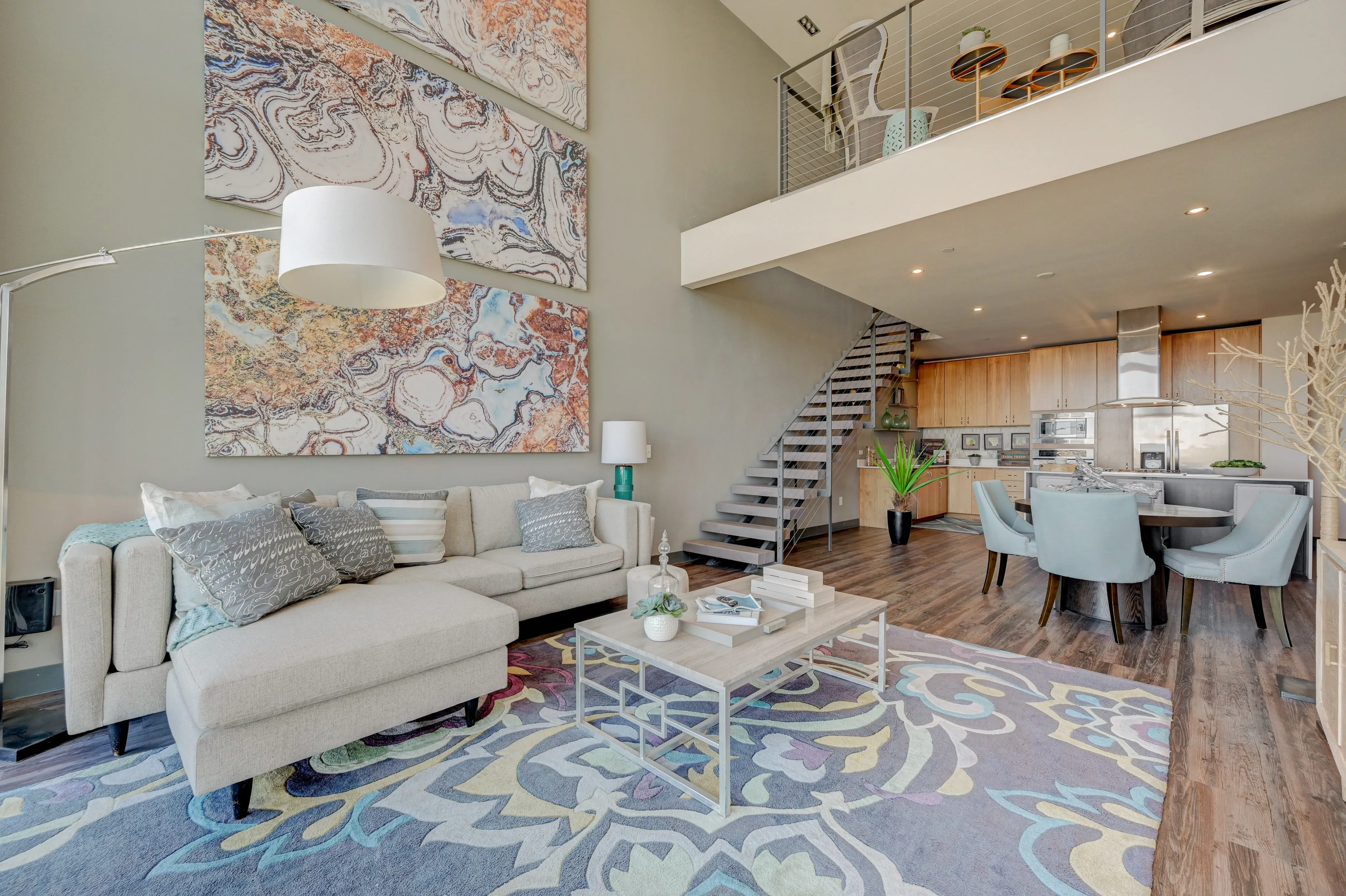 Chic open-concept living area with elegant staircase, modern kitchen, and stylish decor featuring vibrant abstract art.