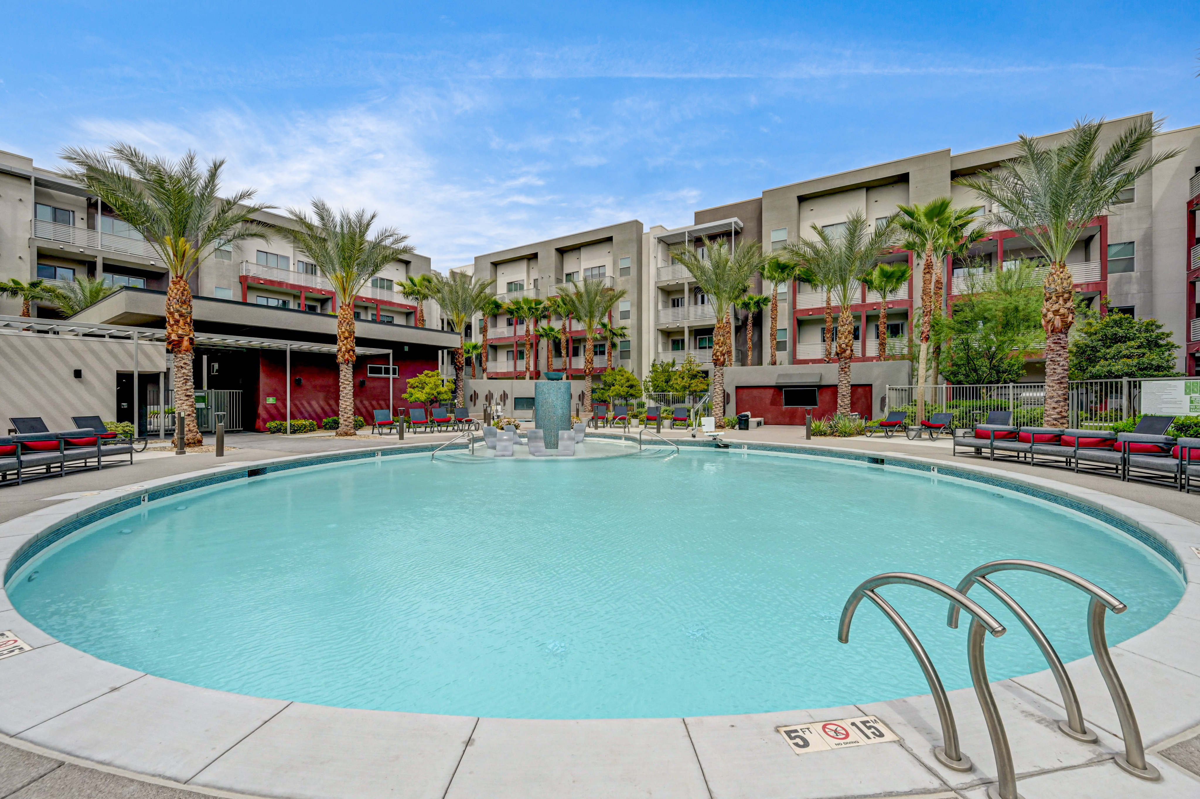 Luxurious apartment complex with a sparkling pool, surrounded by palm trees and modern architecture under a clear blue sky.
