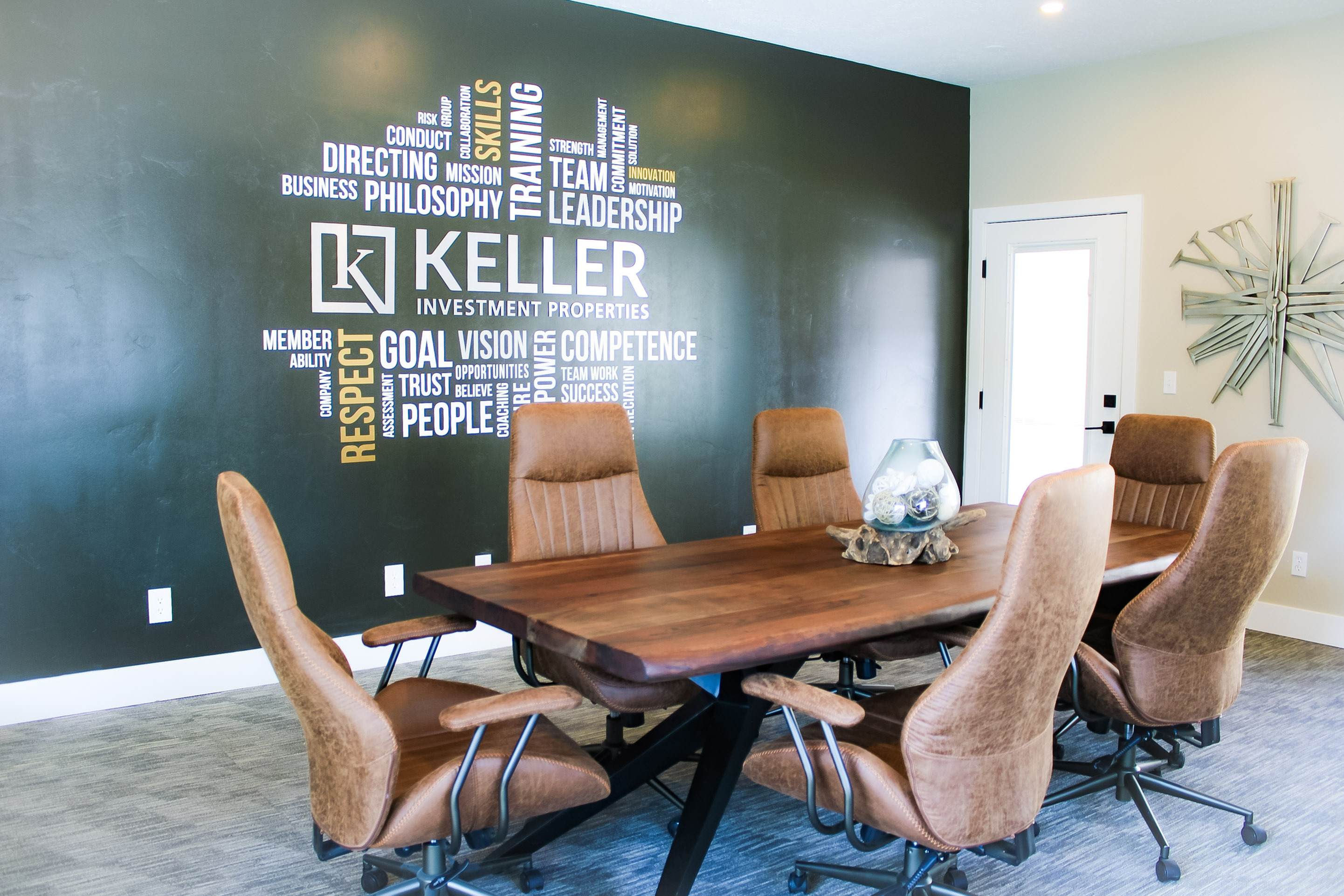 Contemporary conference room with sleek wooden table and modern leather chairs, complemented by an inspirational word cloud wall d&eacute;cor.