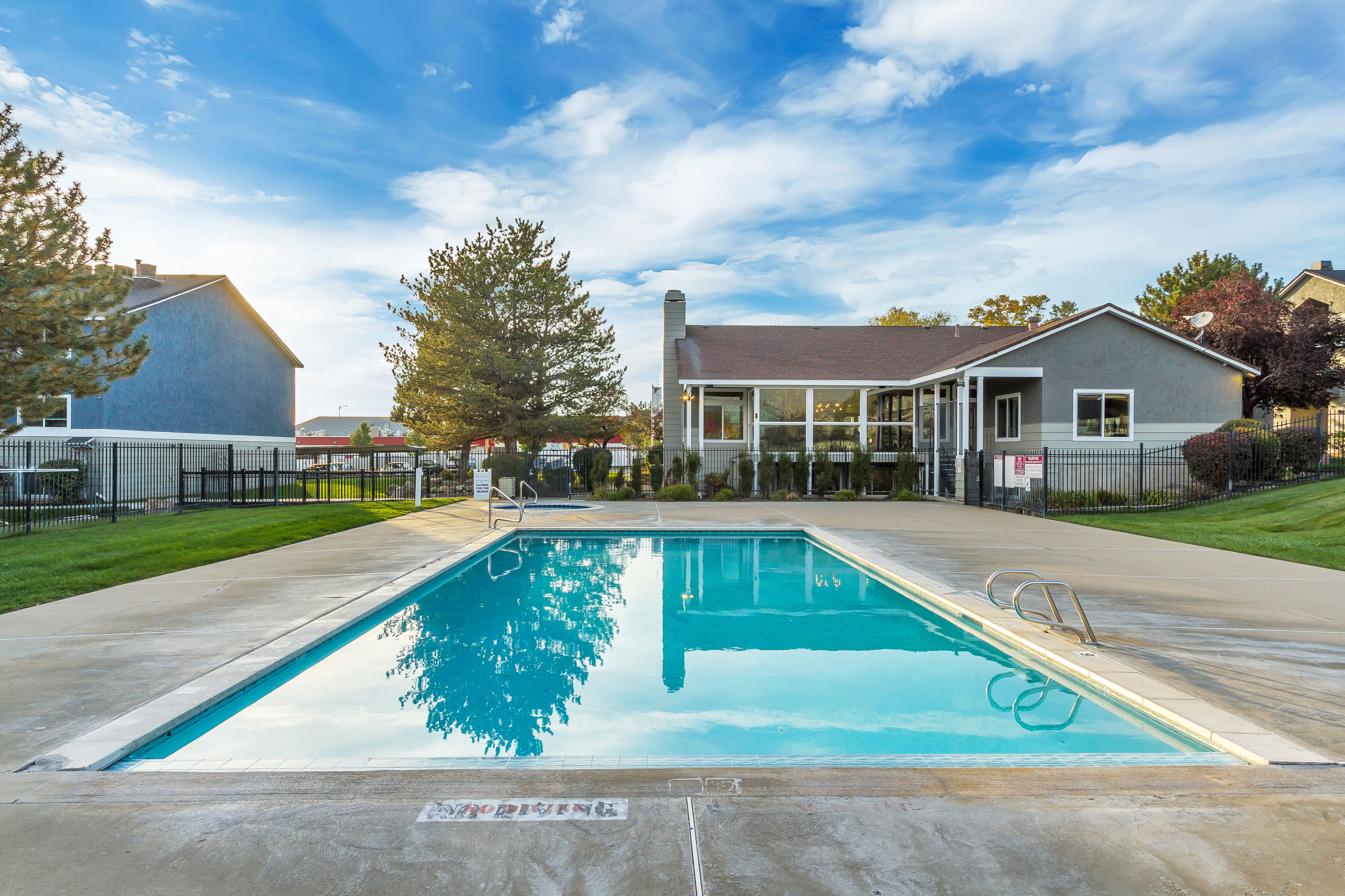 Inviting outdoor pool area with clear blue water, surrounded by lush greenery and a modern clubhouse under a bright blue sky.