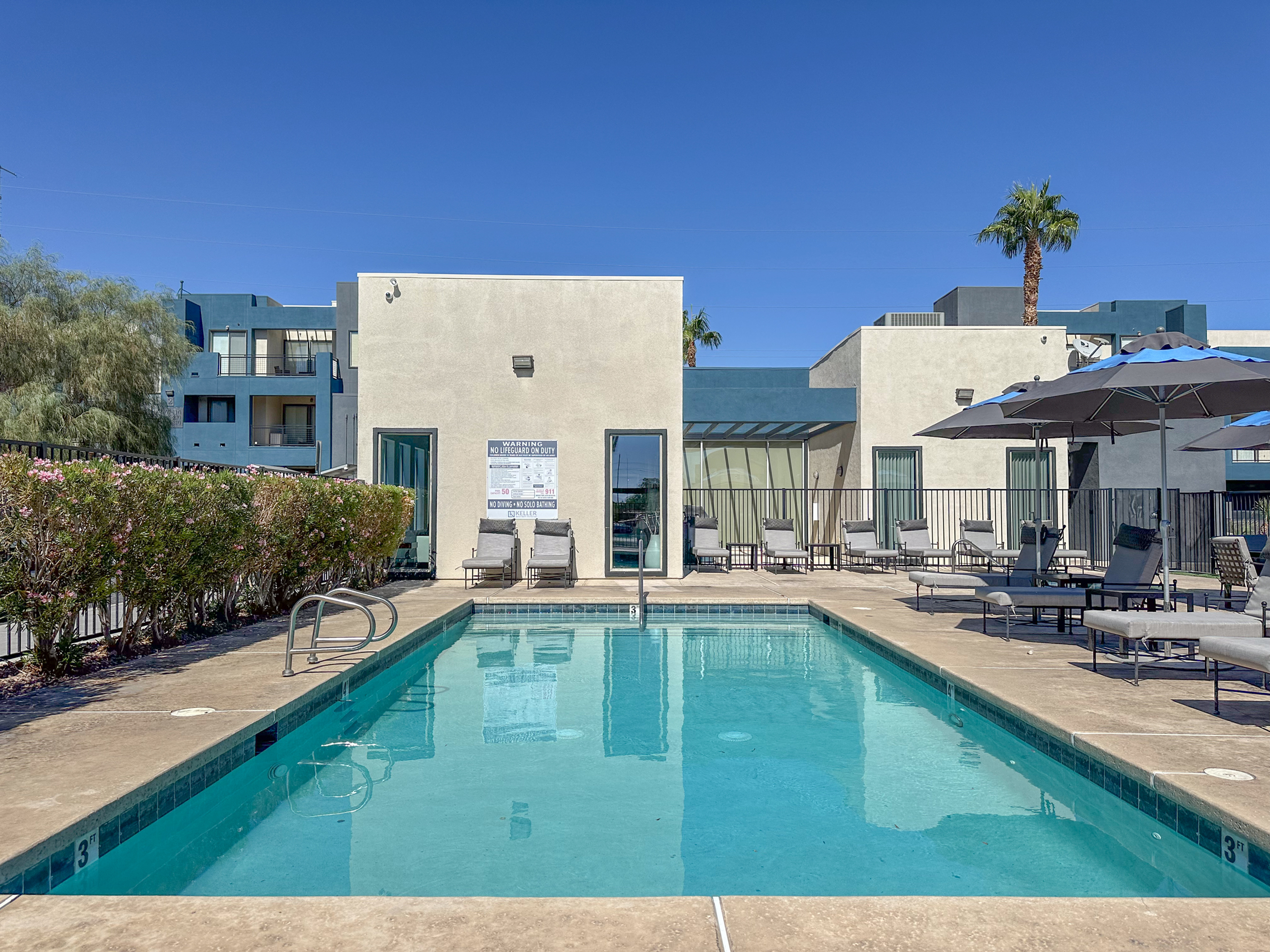 Inviting outdoor pool area with stylish lounge chairs and umbrellas, perfect for relaxation under clear blue skies.