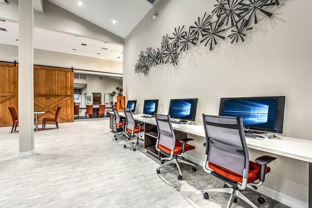 Modern communal workspace with sleek computers, ergonomic chairs, and artistic wall decor, featuring rustic sliding barn doors for a stylish touch.