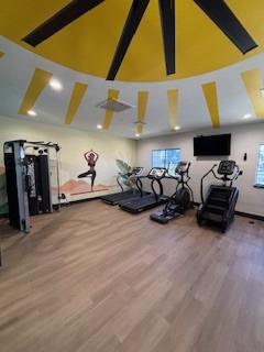 Bright and modern fitness center featuring treadmills, a stair climber, weight machine, and vibrant mural design.