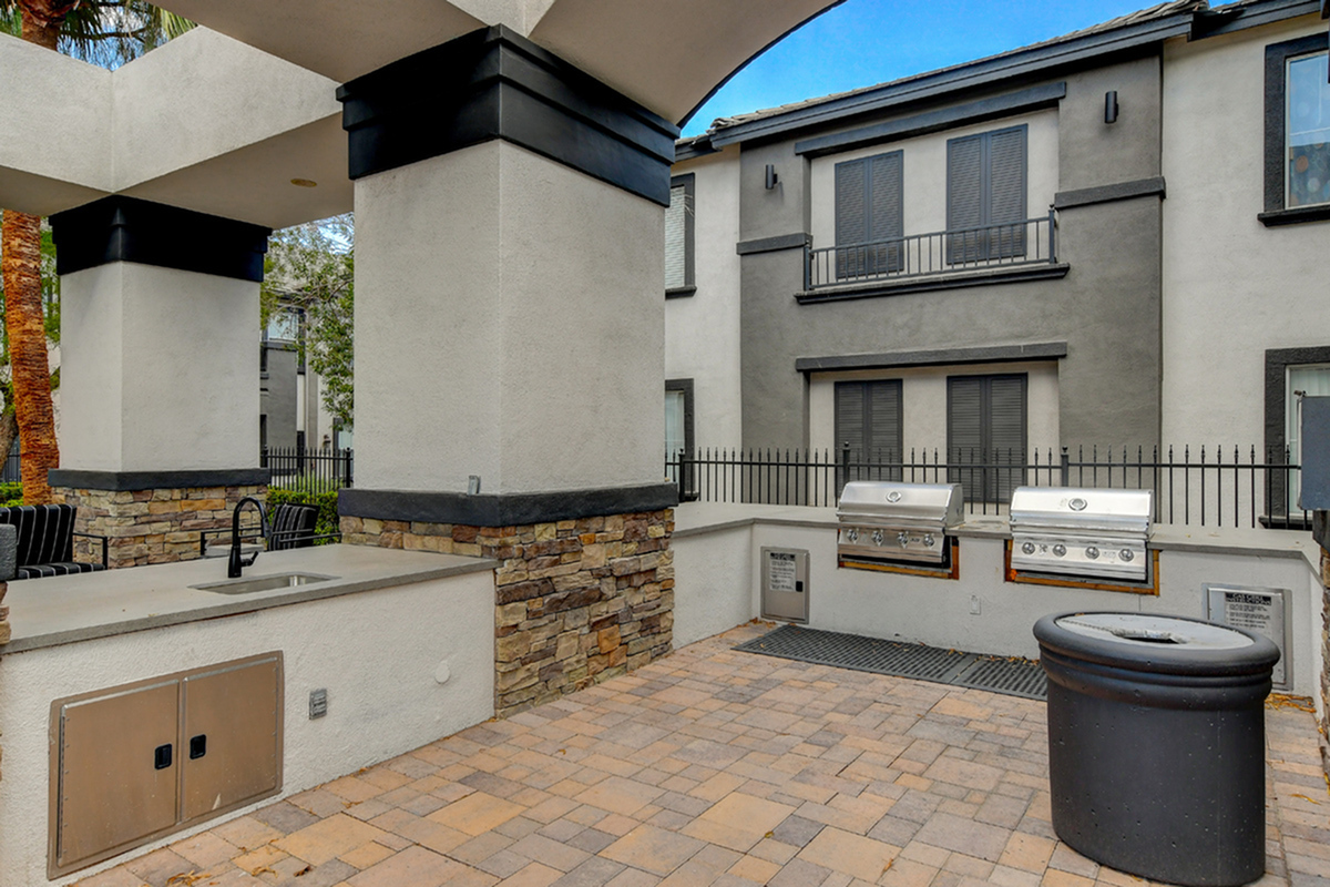Modern outdoor barbecue area with twin stainless steel grills, elegant stone counters, and cozy seating in a stylish apartment complex.