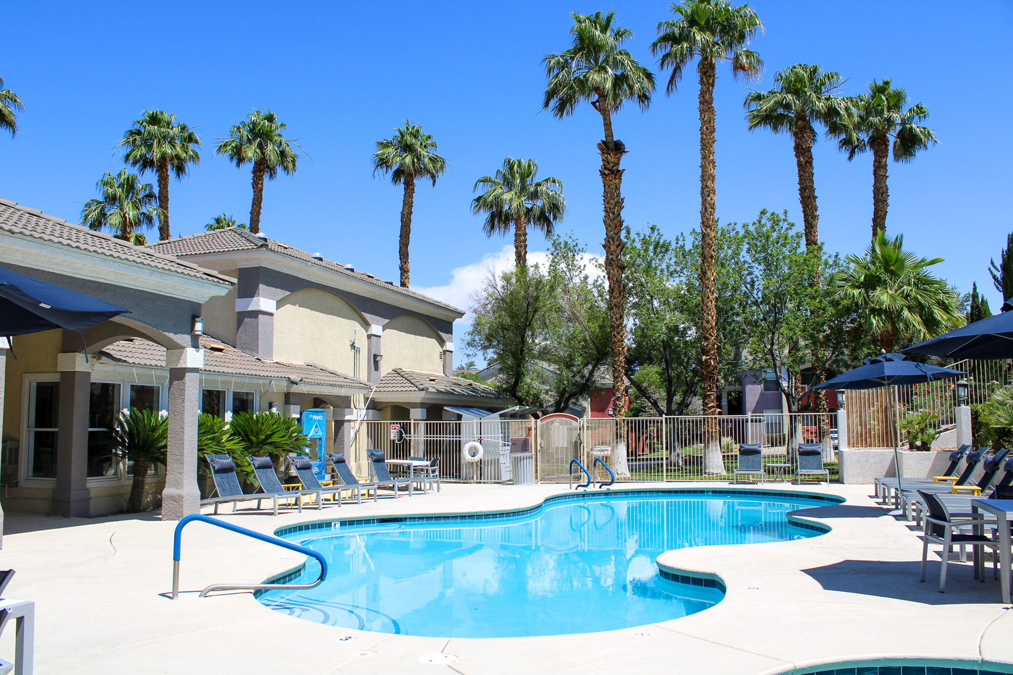 Luxurious apartment complex featuring a stunning pool surrounded by palm trees and sun loungers, perfect for relaxation and leisure.