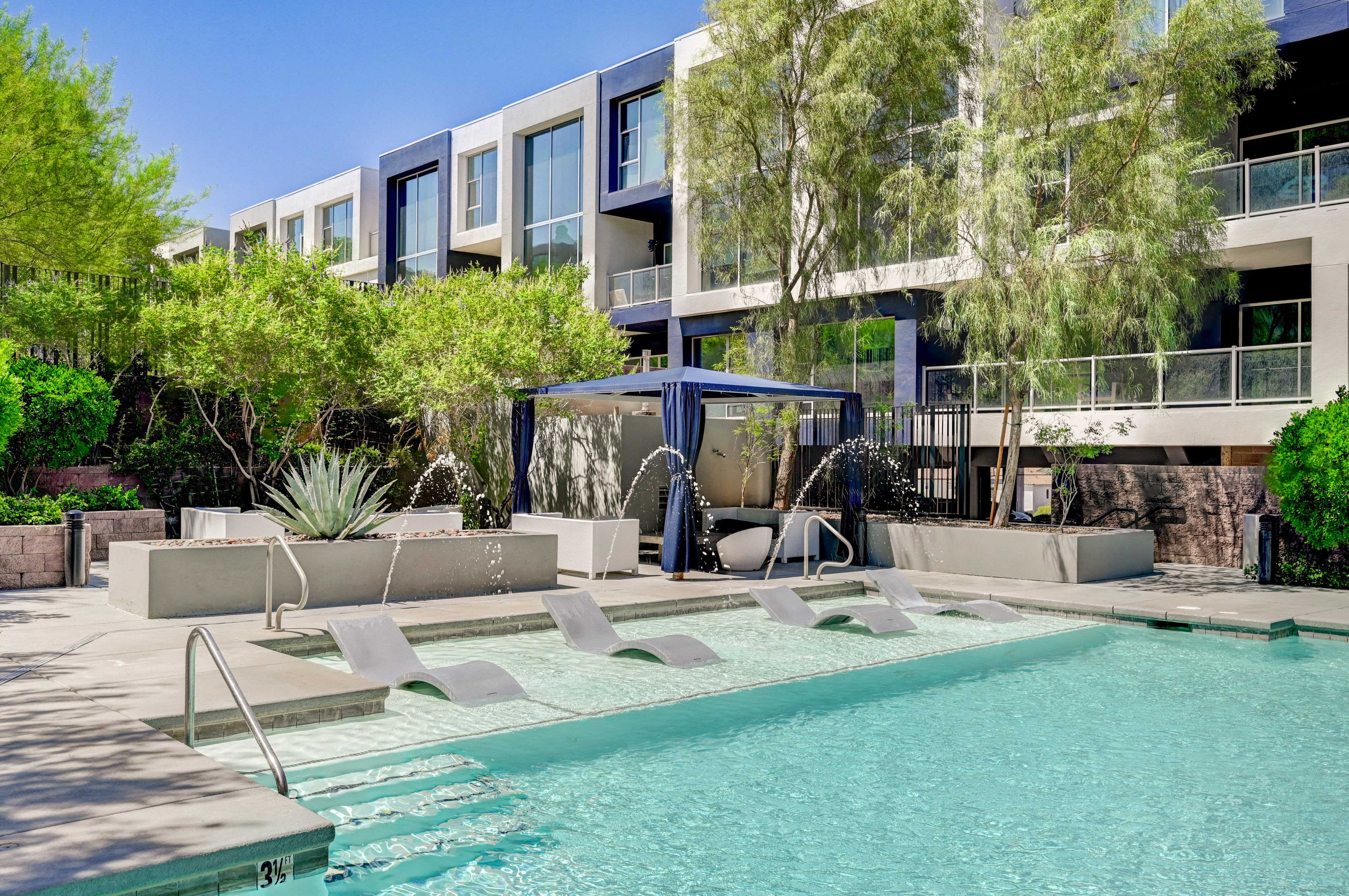 Luxurious modern apartment complex with a pristine outdoor pool, elegant cabanas, and lush greenery, perfect for relaxing and entertaining.