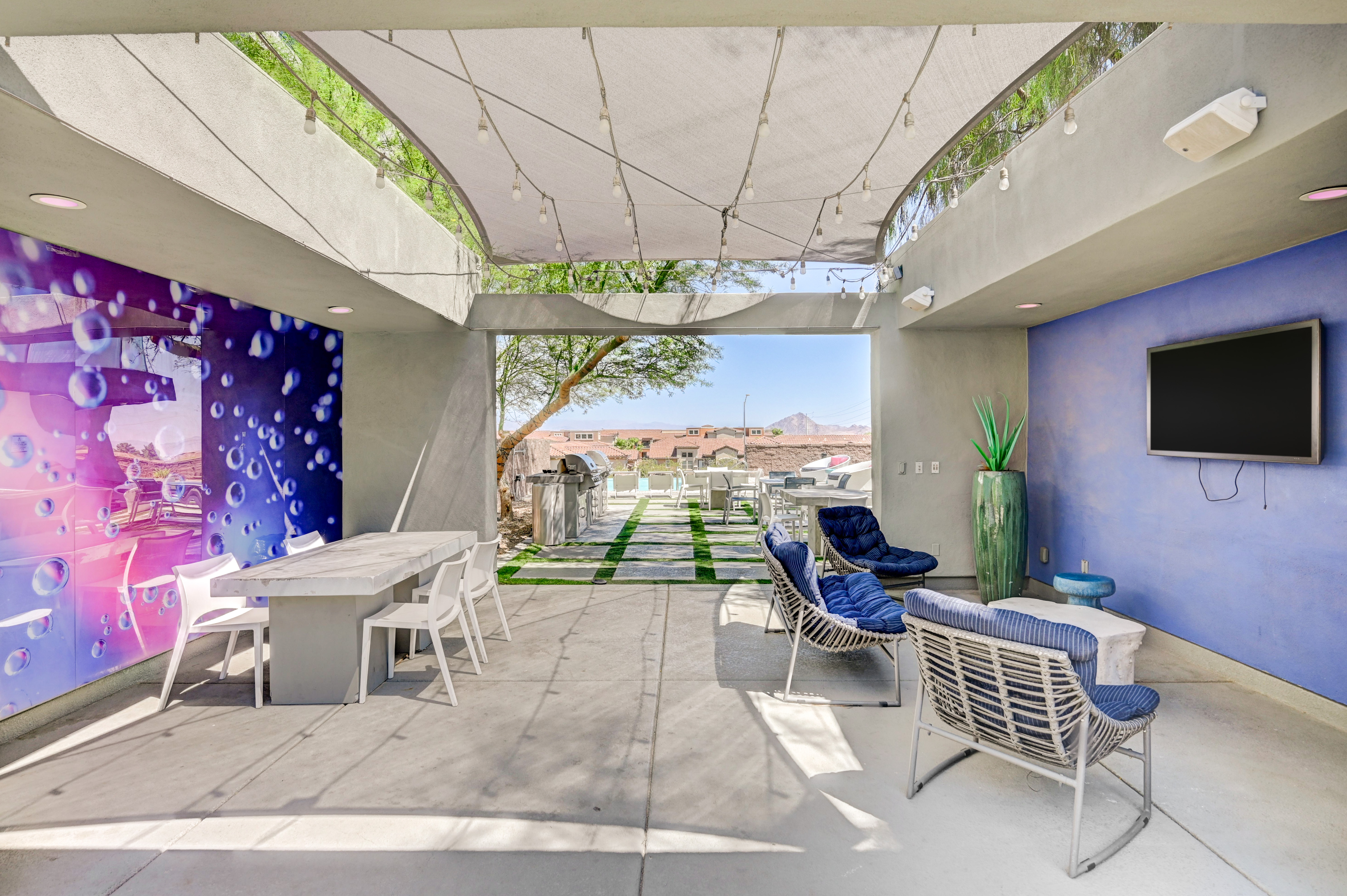 Chic outdoor dining and lounging area with vibrant wall art, modern seating, and picturesque views under stylish shade sails.