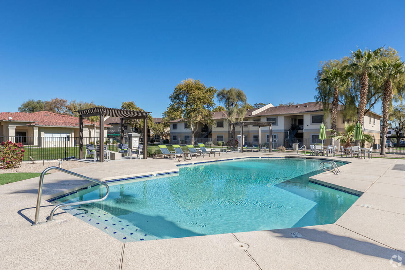 Inviting outdoor pool area with sun loungers, surrounded by lush palm trees and well-maintained landscaping, perfect for relaxation in a vibrant community setting.
