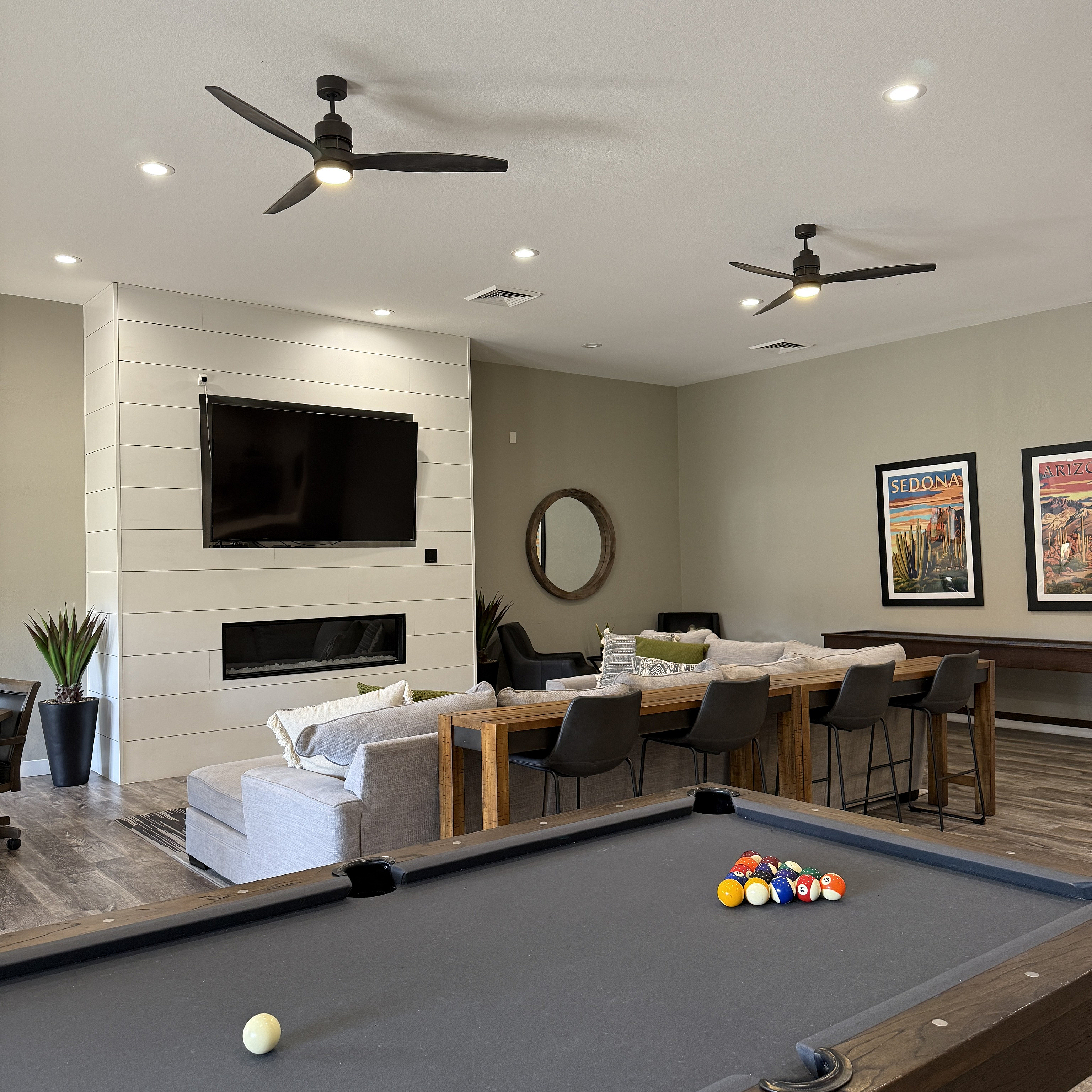 Modern lounge area with a sleek pool table, stylish bar seating, and contemporary ceiling fans offering a chic entertainment space.