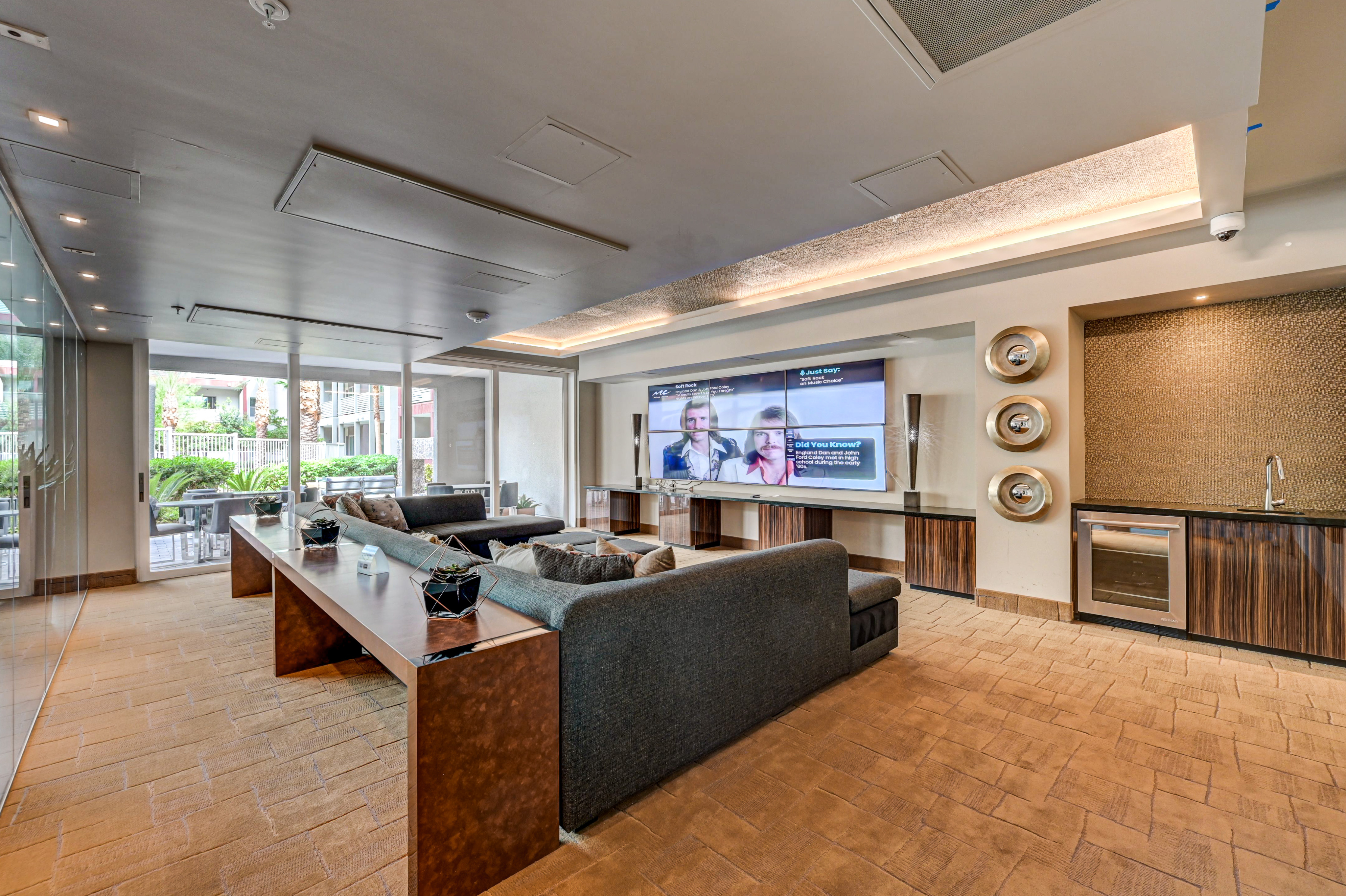 Elegant lounge area featuring plush seating, a large TV, and modern decor with a view of lush garden surroundings.