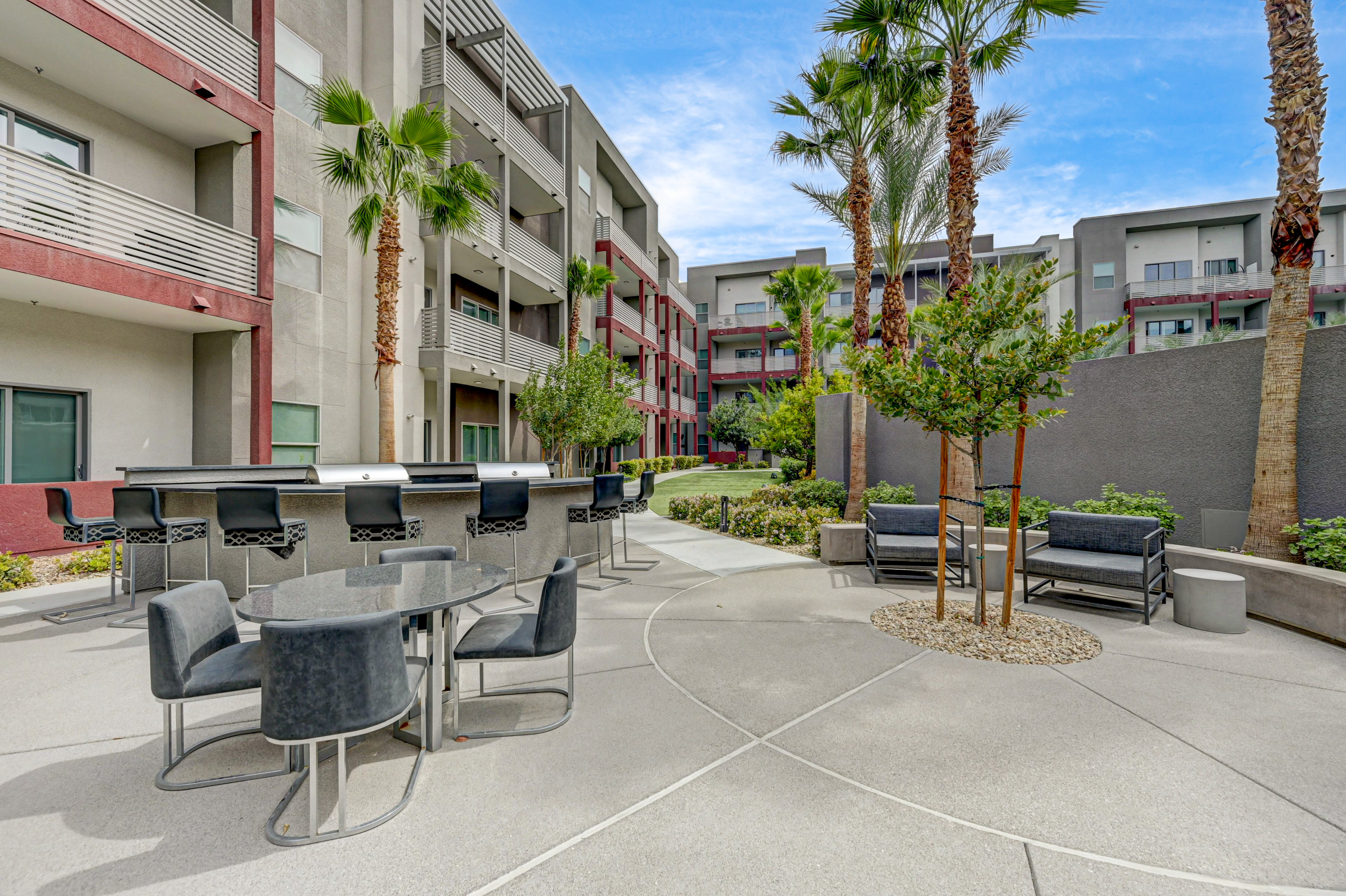 Modern apartment courtyard featuring sleek outdoor seating, palm trees, and stylish communal grilling area.