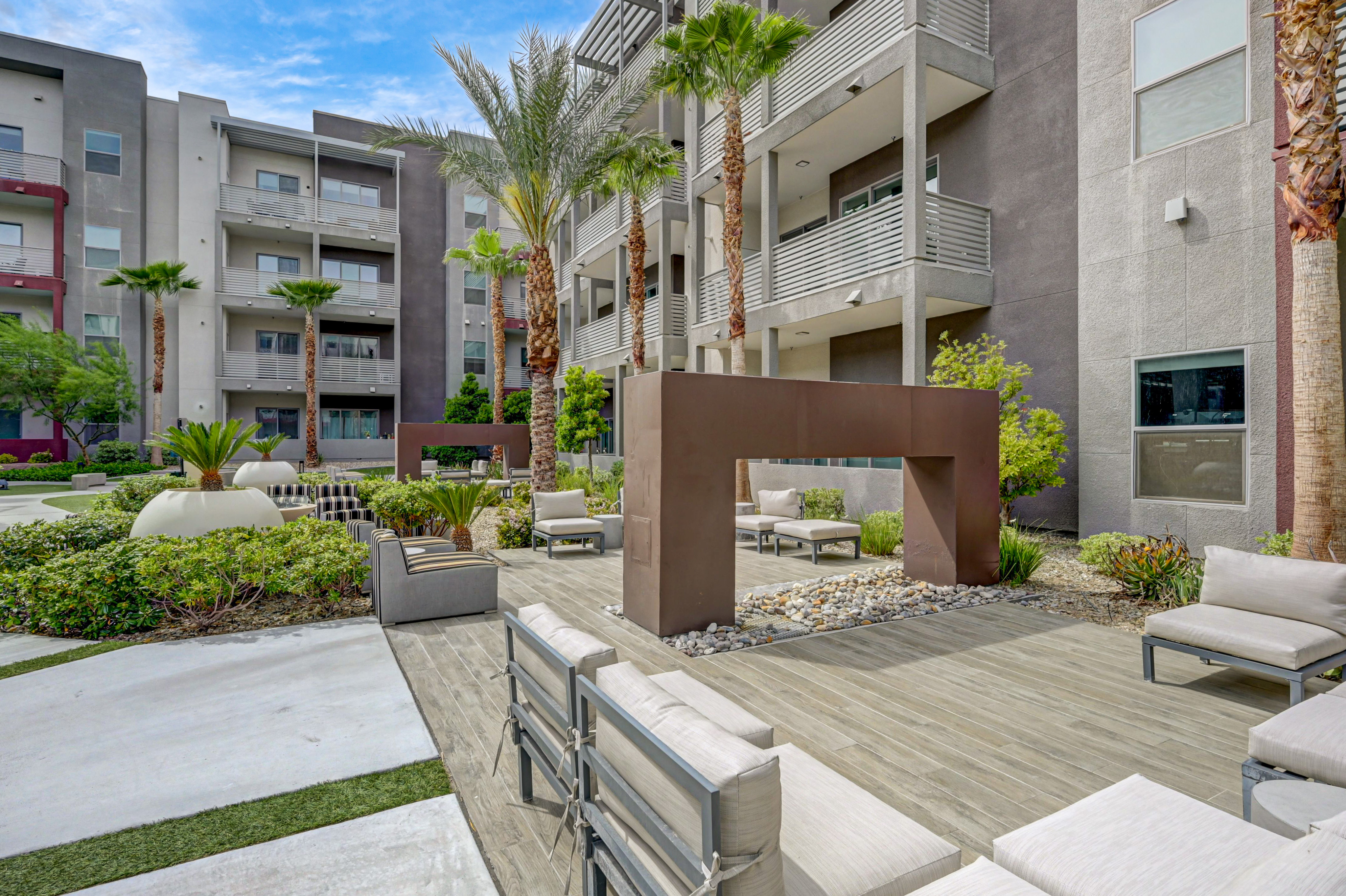Modern apartment complex courtyard featuring stylish seating, lush greenery, and palm trees, creating a relaxing outdoor oasis.