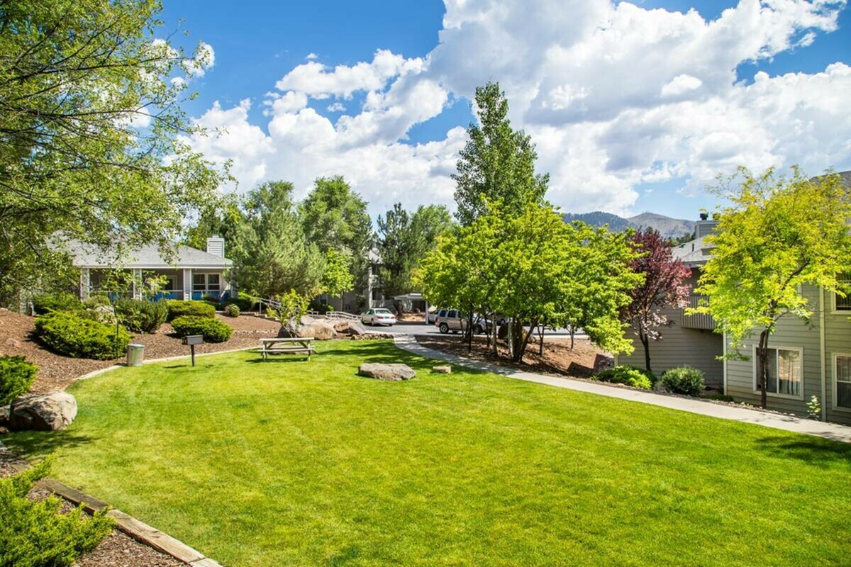 Charming apartment community with lush green lawn, mature trees, and stunning mountain views.