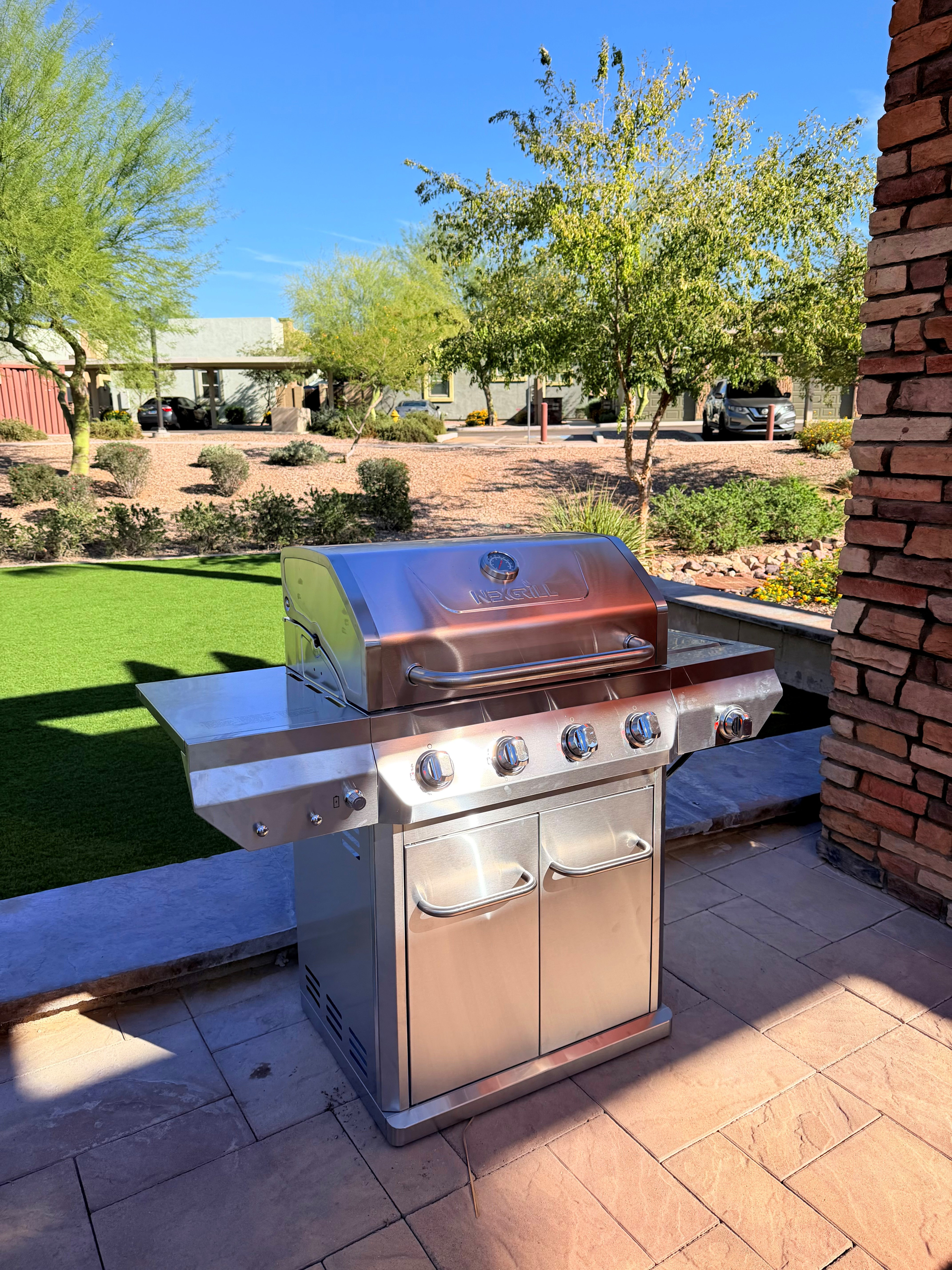 Modern outdoor space featuring a sleek stainless steel BBQ grill, surrounded by lush greenery and elegant stonework.