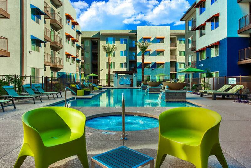 Chic apartment complex featuring a stunning outdoor pool area with vibrant chairs and modern architecture under a clear blue sky.