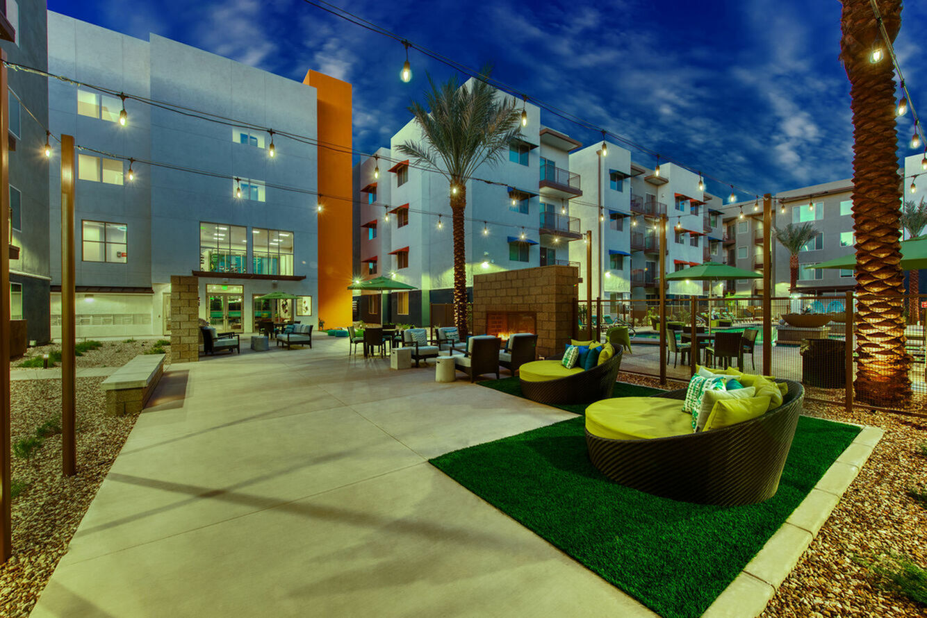Vibrant apartment courtyard featuring modern seating, cozy fire pit, and lush greenery under string lights.