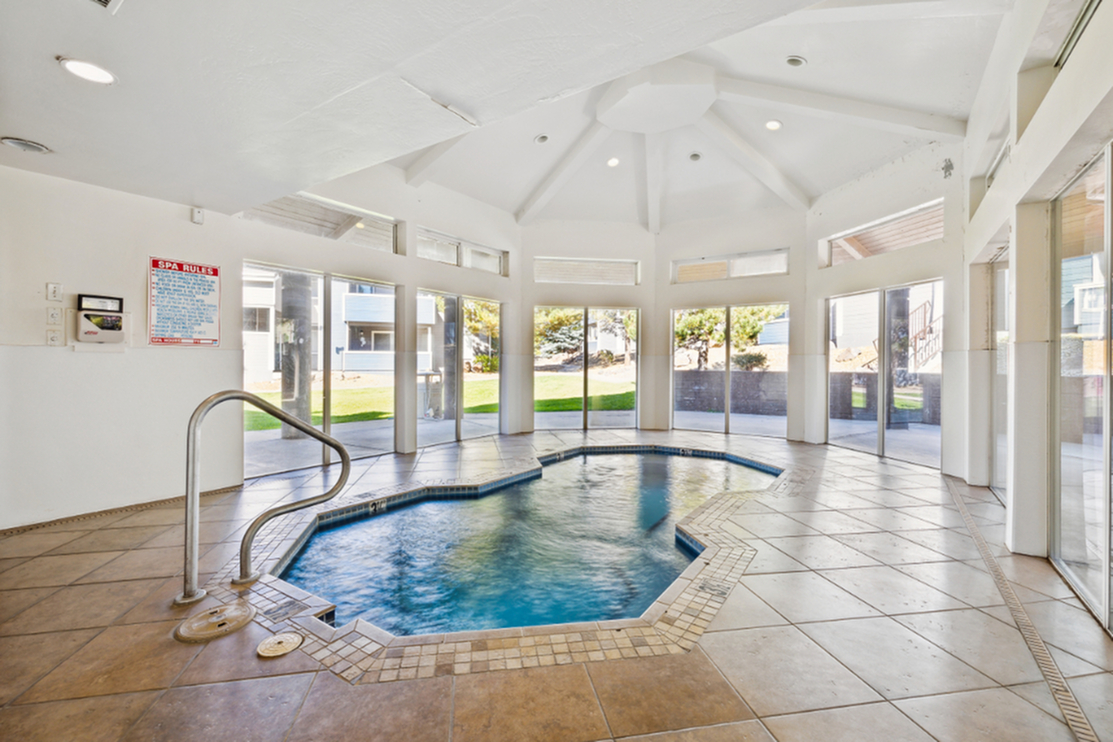 Bright indoor spa retreat with modern hexagonal hot tub and panoramic windows overlooking lush greenery.