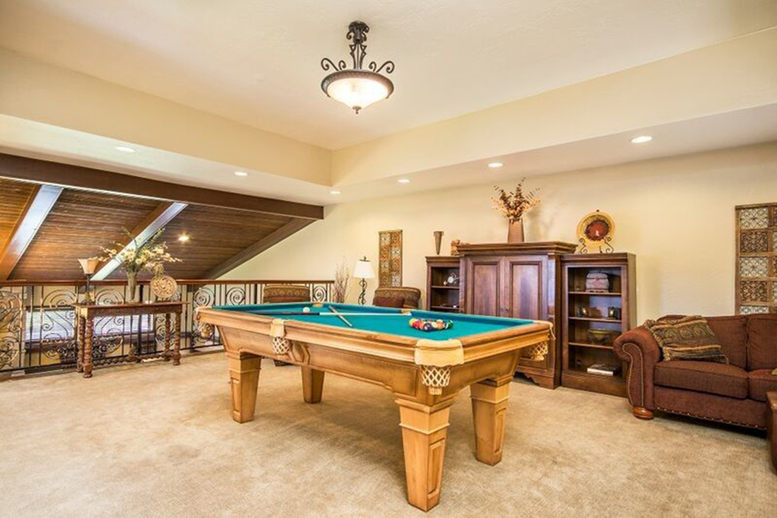 Luxurious loft space featuring a classic billiard table, cozy sofa, and elegant wooden furniture, perfect for entertainment and relaxation.