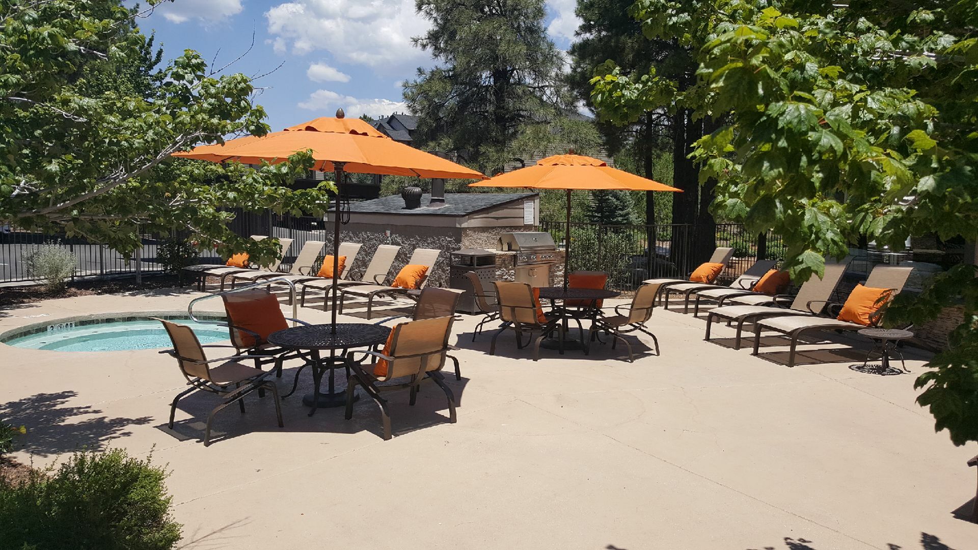 Inviting outdoor patio with a pristine pool, vibrant orange umbrellas, and comfortable loungers under lush greenery.