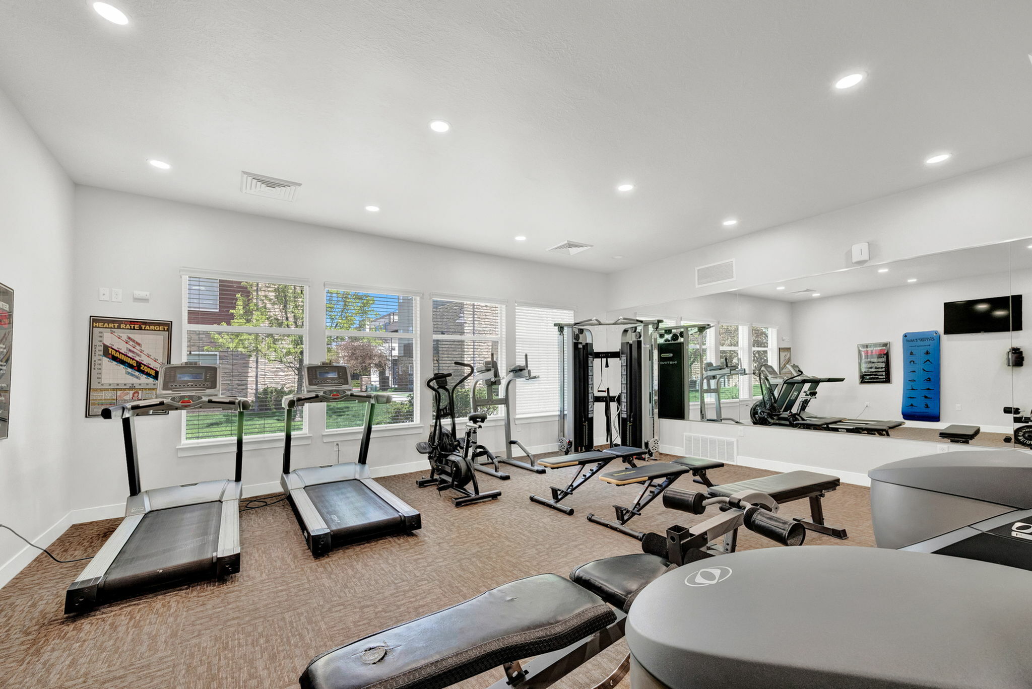 Bright and modern fitness center equipped with treadmills, elliptical machines, and strength training equipment, offering a dynamic workout experience with natural light streaming through large windows.