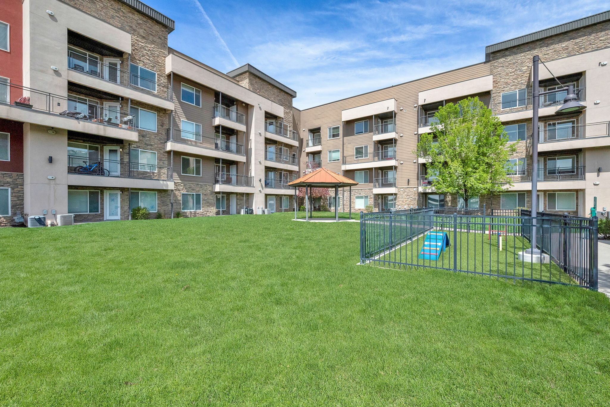 Charming apartment complex featuring spacious balconies, lush green courtyard, and a cozy gazebo, perfect for relaxation and community gatherings.