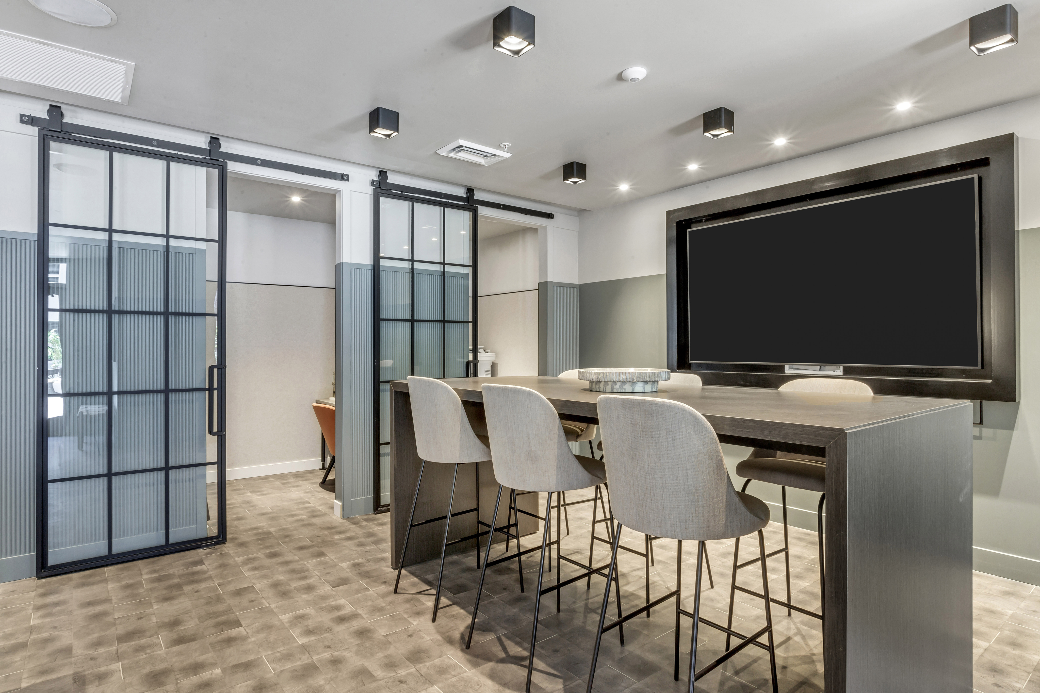 Modern apartment meeting space with sleek sliding glass doors, stylish bar stools, and a large built-in screen.