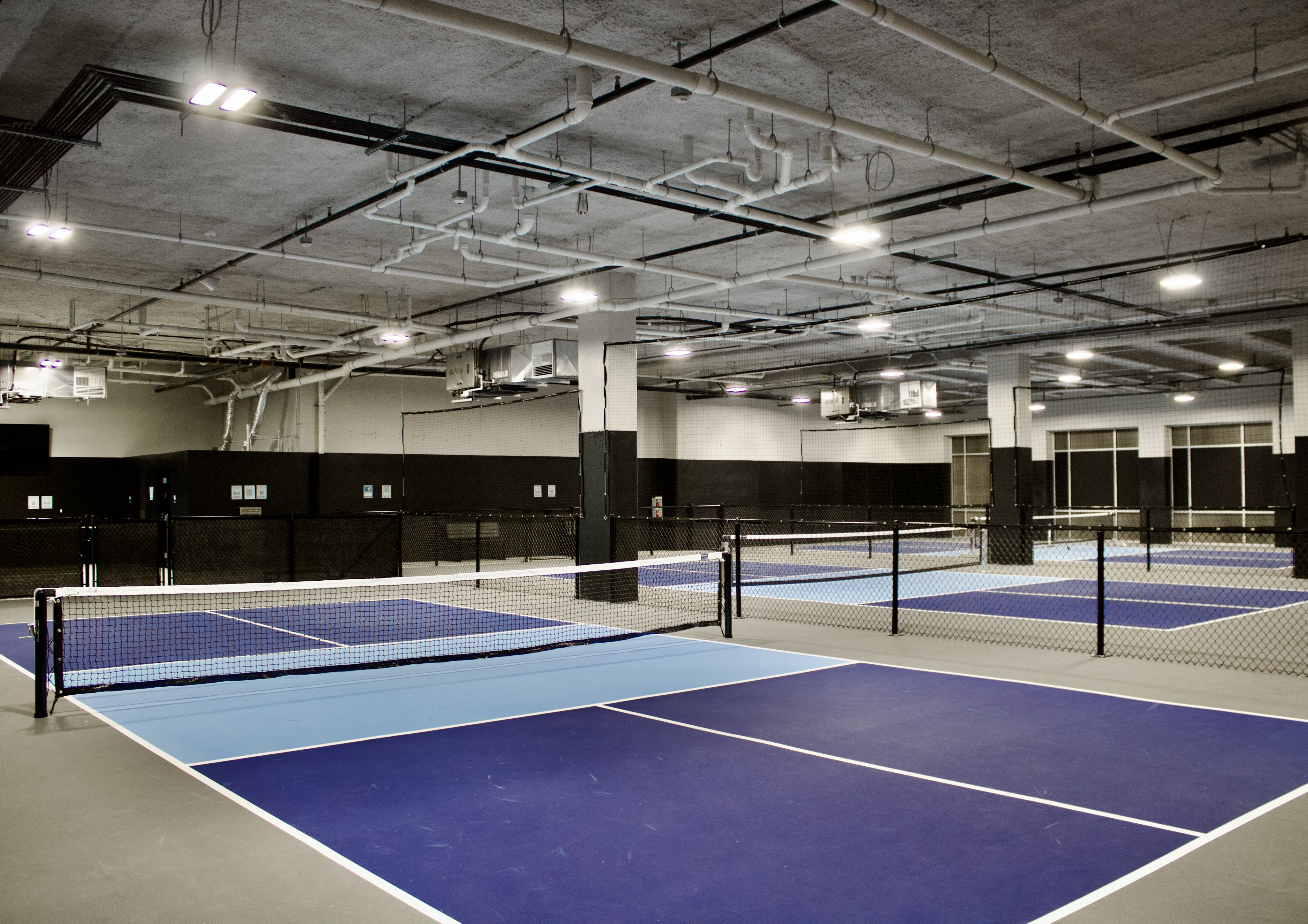 State-of-the-art indoor tennis court with modern lighting and vibrant blue flooring, ideal for recreational and competitive play.