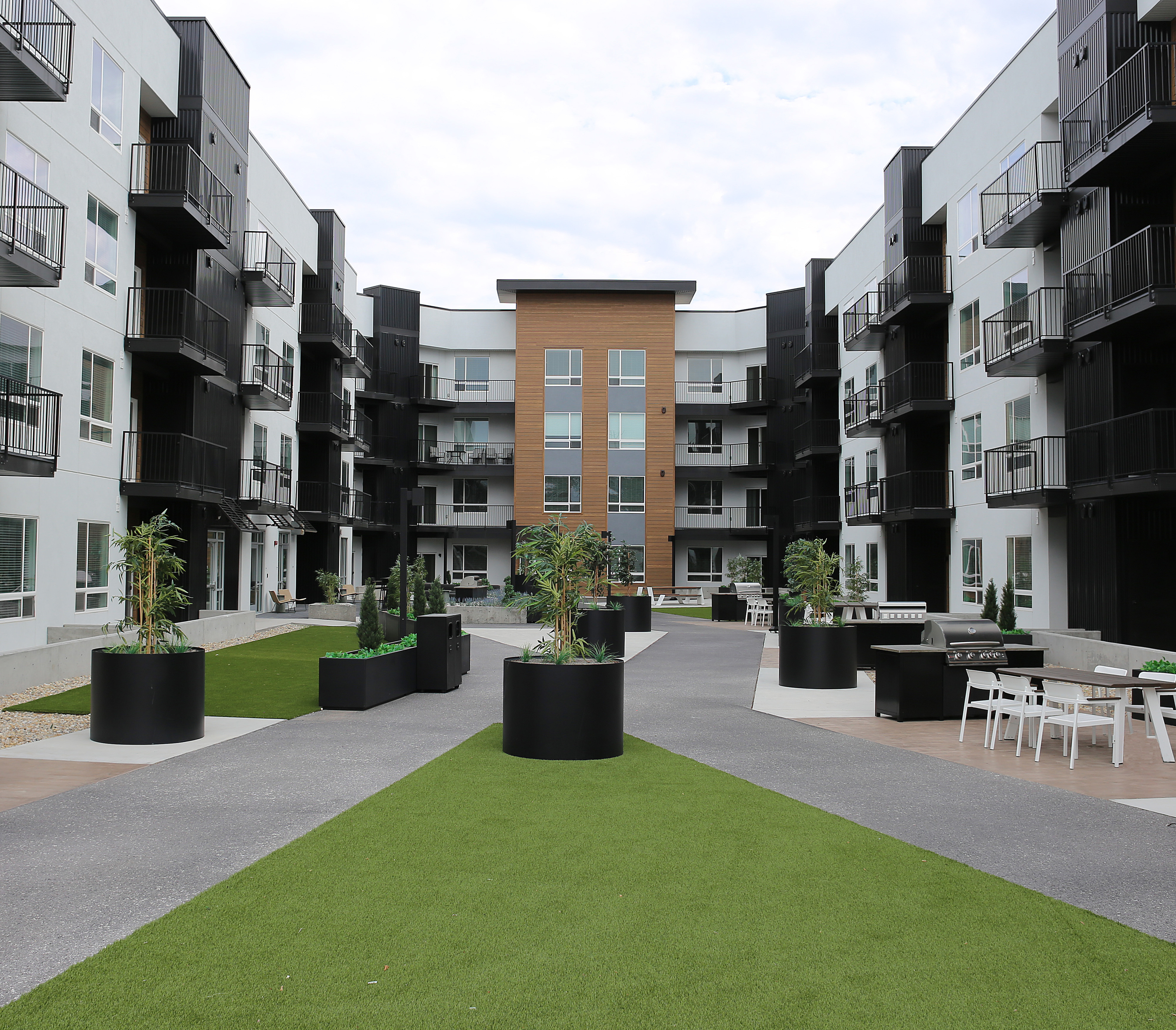 Modern apartment complex featuring contemporary architecture with spacious balconies, lush greenery, and inviting outdoor seating areas.