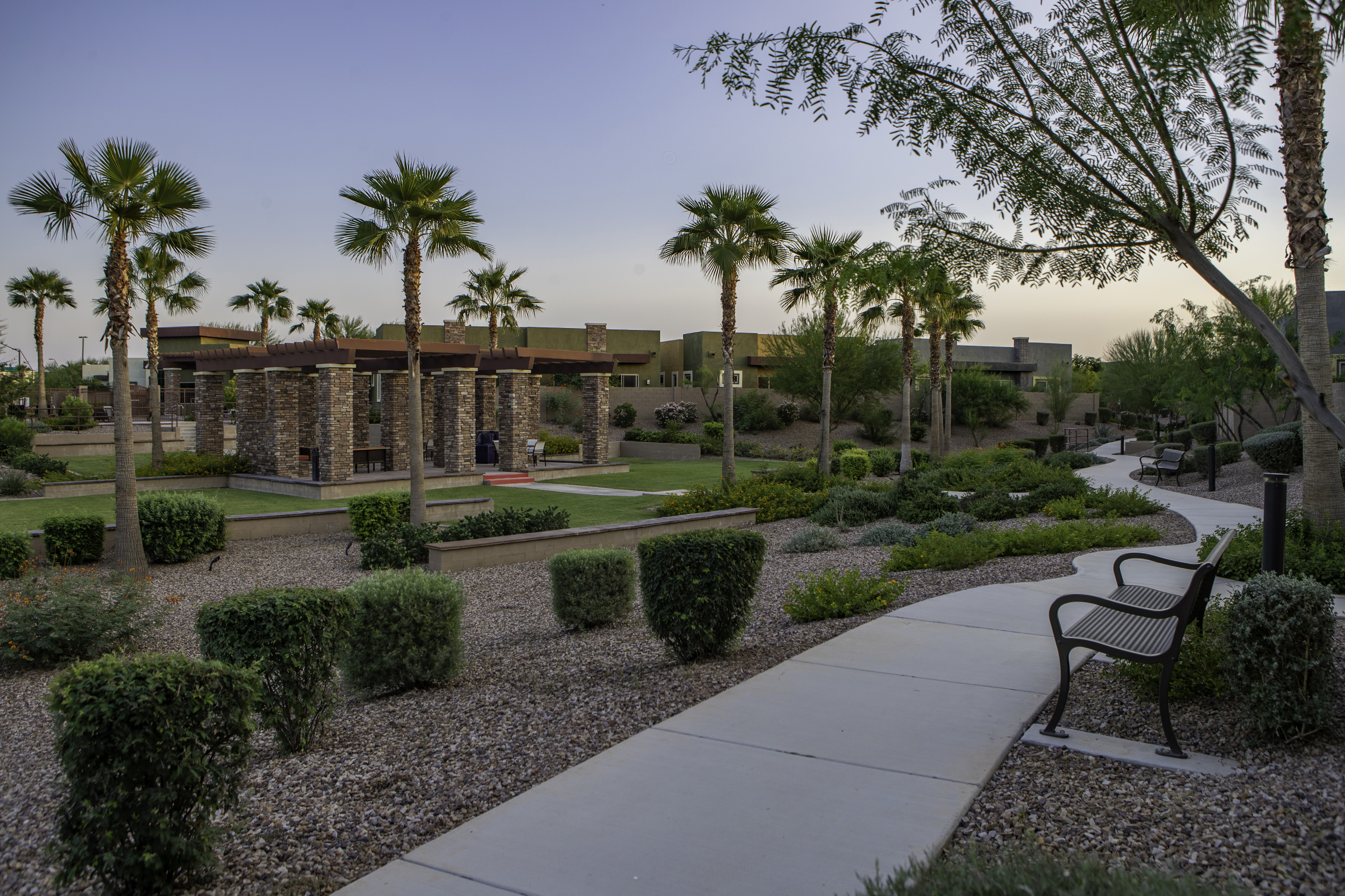 Serene pathway with lush landscaping and elegant stone gazebos surrounded by palm trees in a tranquil garden setting.