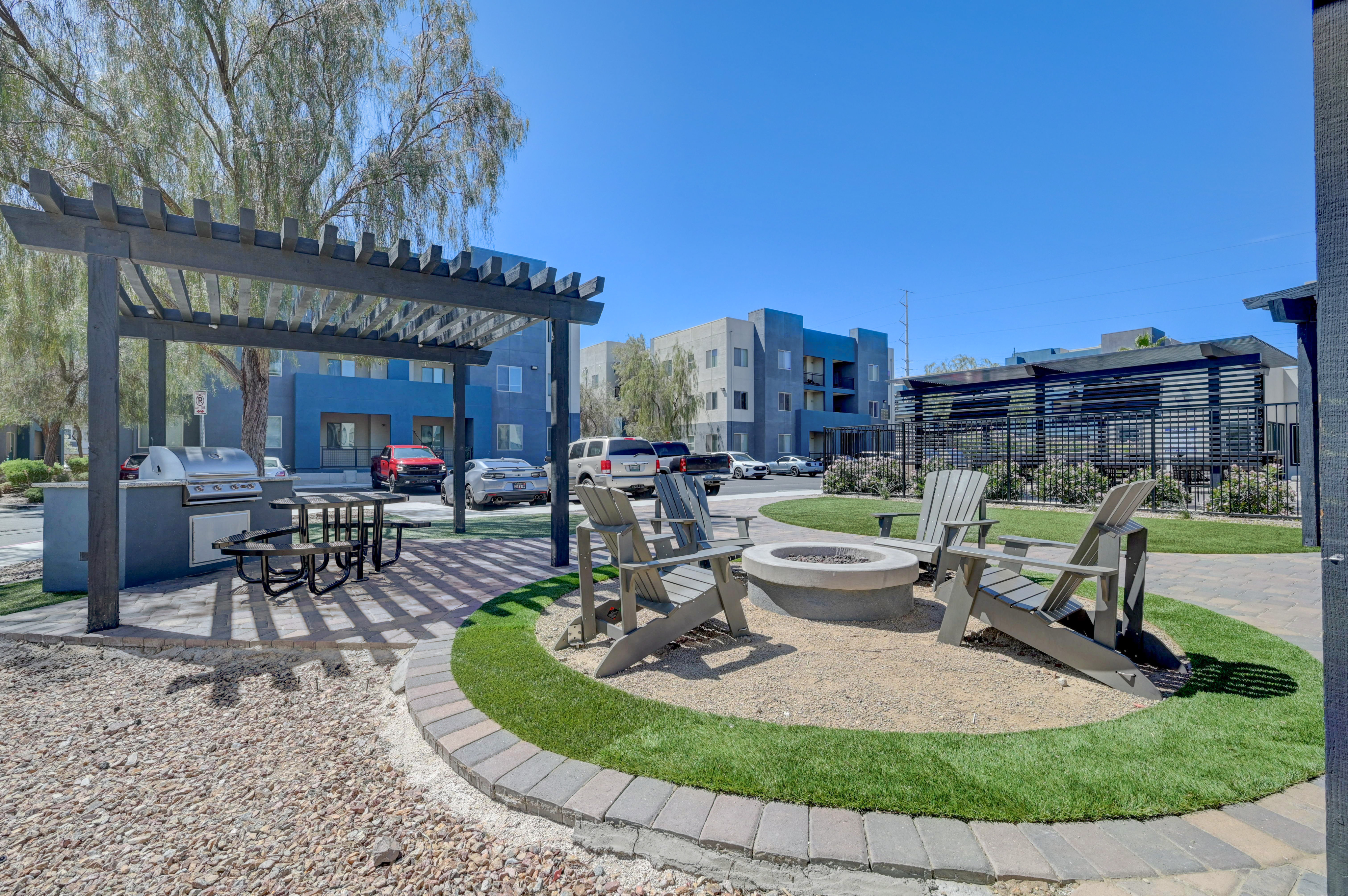 Modern apartment complex with serene outdoor space featuring a pergola, barbecue area, and cozy fire pit surrounded by seating, perfect for relaxation and gatherings.