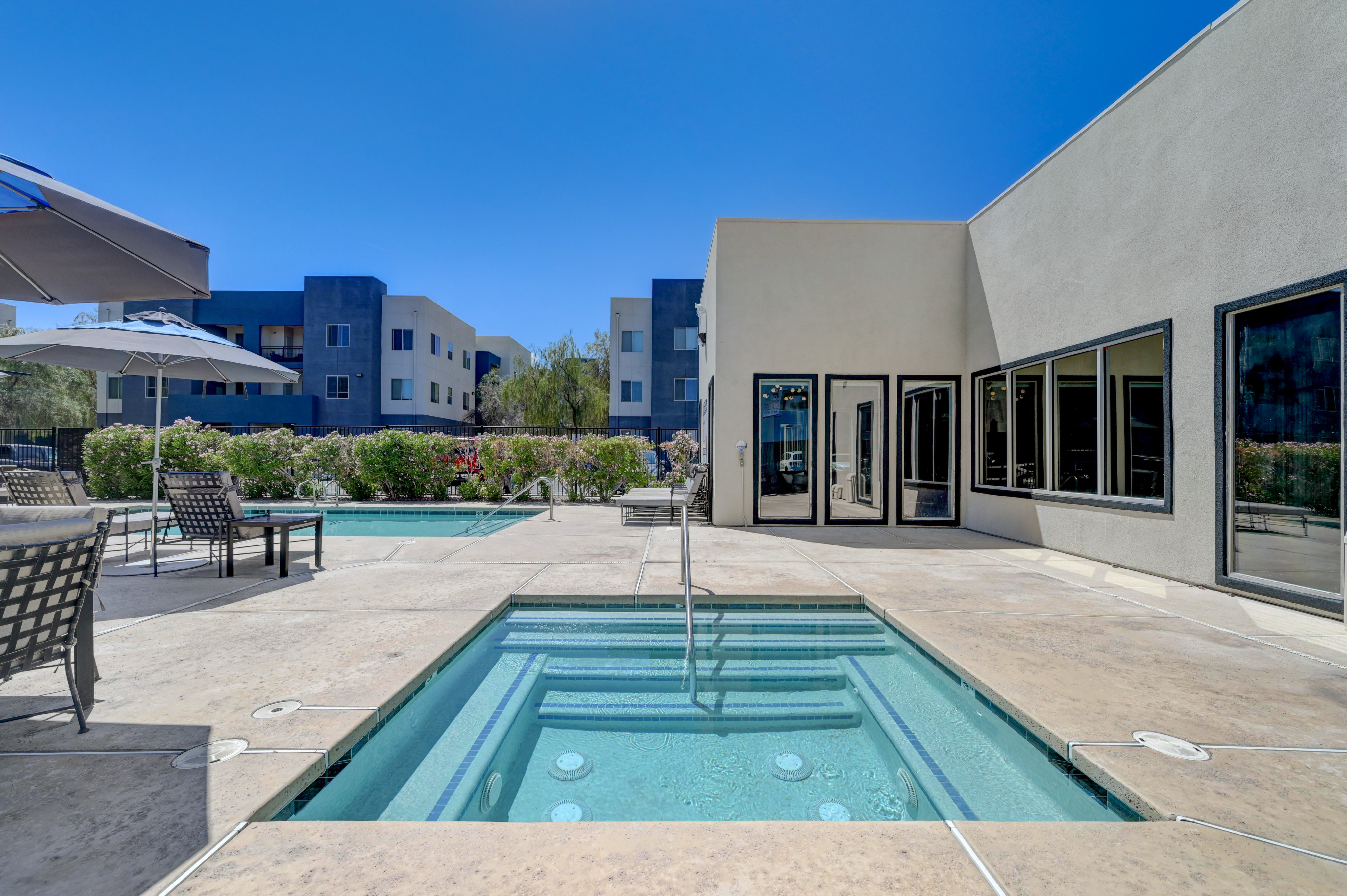 Elegant apartment complex featuring a refreshing swimming pool and cozy patio area, perfect for relaxation and outdoor enjoyment on a sunny day.