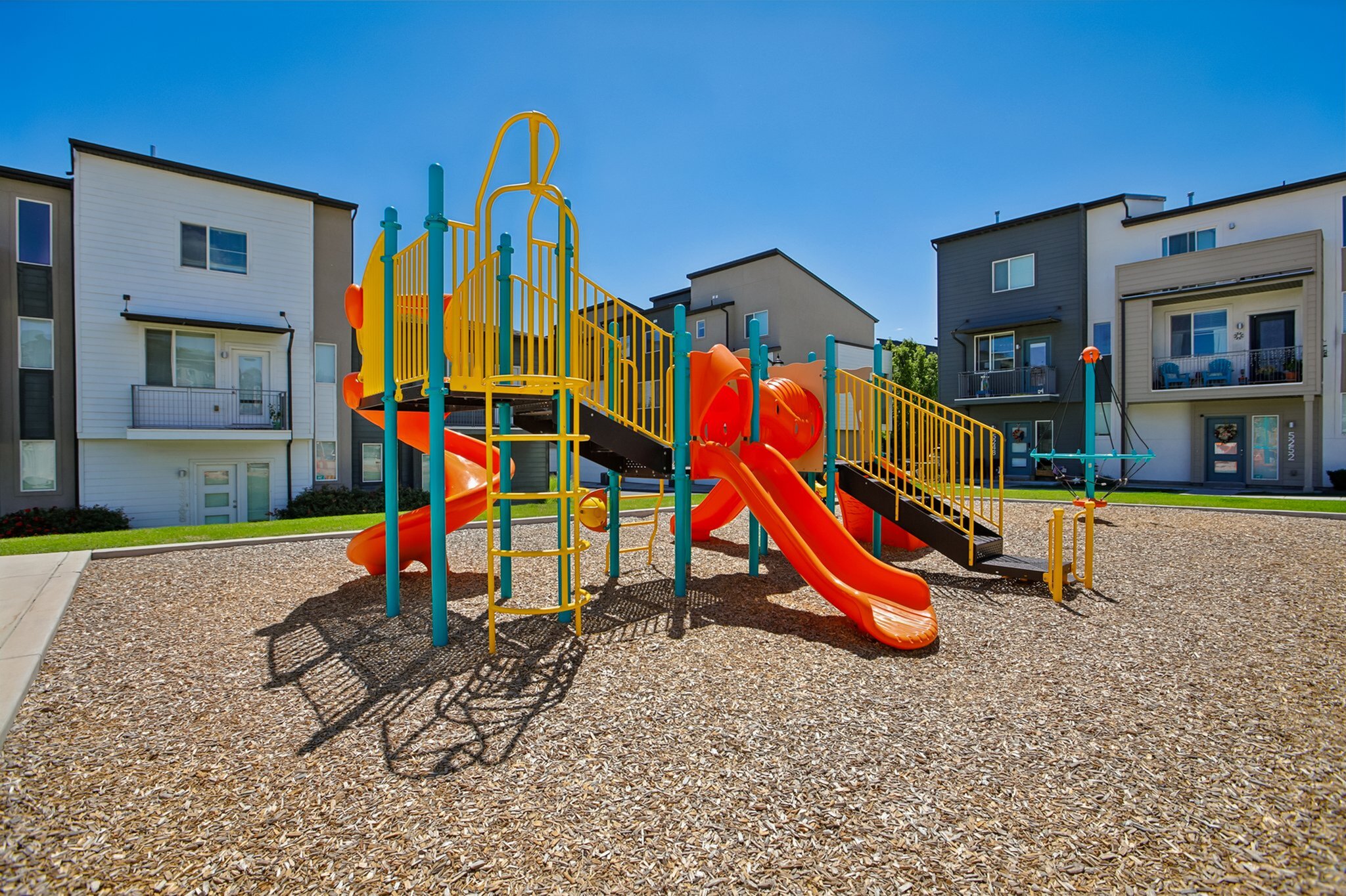 Charming apartment complex with vibrant playground, featuring colorful slides and climbing structures, ideal for family-friendly living.