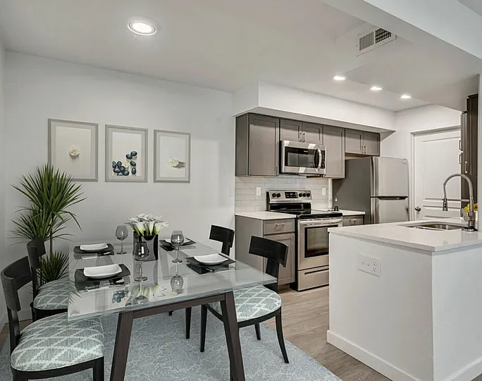 Modern open-plan apartment kitchen with sleek stainless steel appliances, a glass dining table, and stylish decor.
