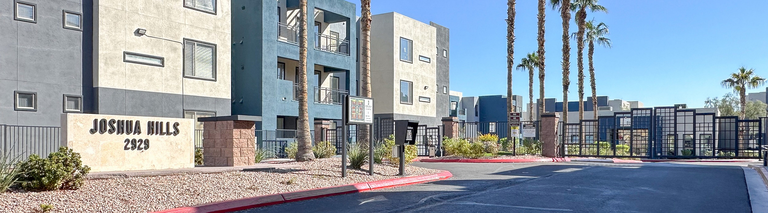 Elegant apartment complex entrance at Joshua Hills, showcasing modern architecture with palm trees lining the entrance path.