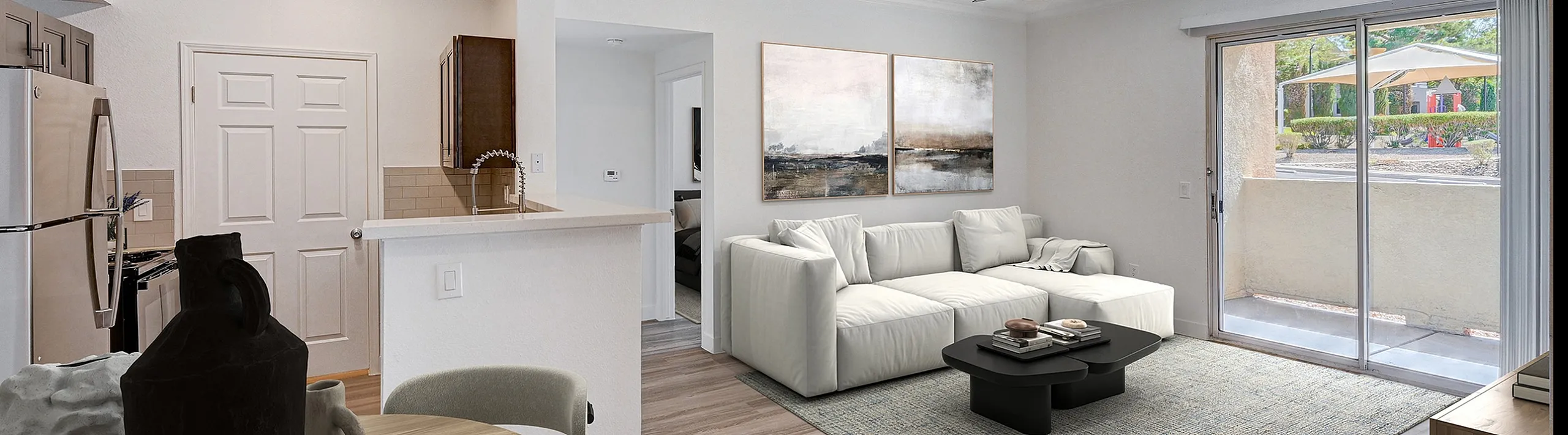 Bright and modern open-concept living space featuring a sleek kitchen, cozy living area with a plush sofa, and a large sliding glass door leading to a lush outdoor view.