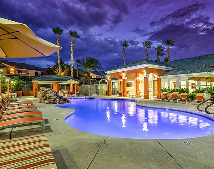 Luxurious apartment complex at sunset featuring an inviting illuminated pool, stylish lounge chairs, and elegant landscaping.