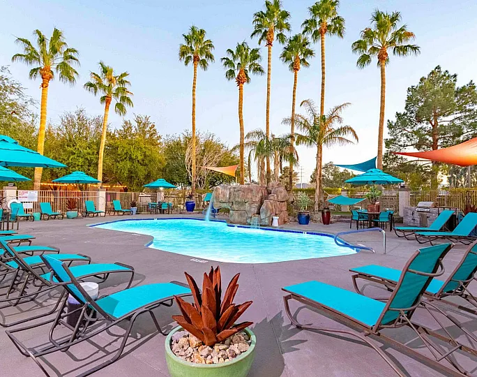 Inviting outdoor swimming pool area surrounded by lush palm trees and vibrant turquoise lounge chairs, perfect for relaxation and leisure.