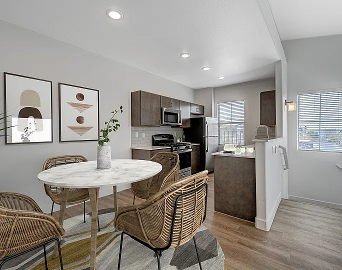 Bright open-concept dining area with elegant wicker chairs and modern kitchen, showcasing stylish decor and abundant natural light.