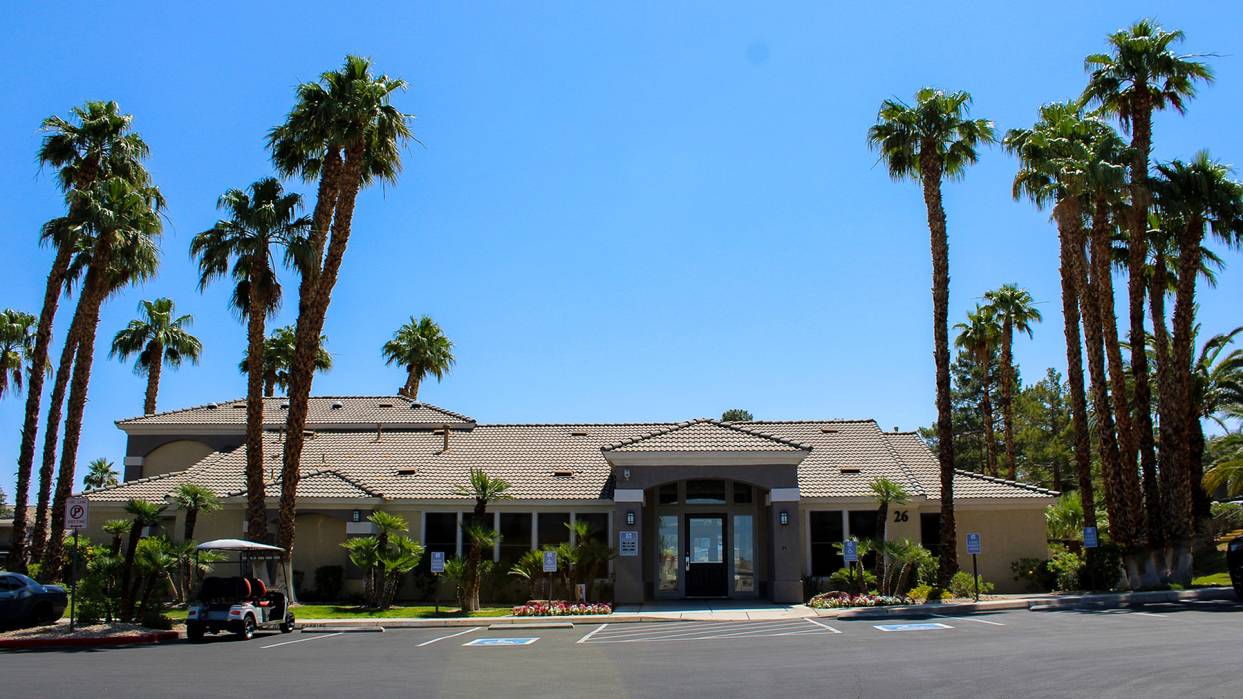 Elegant apartment building entrance surrounded by tall palm trees and a clear blue sky, offering a tropical and inviting atmosphere.