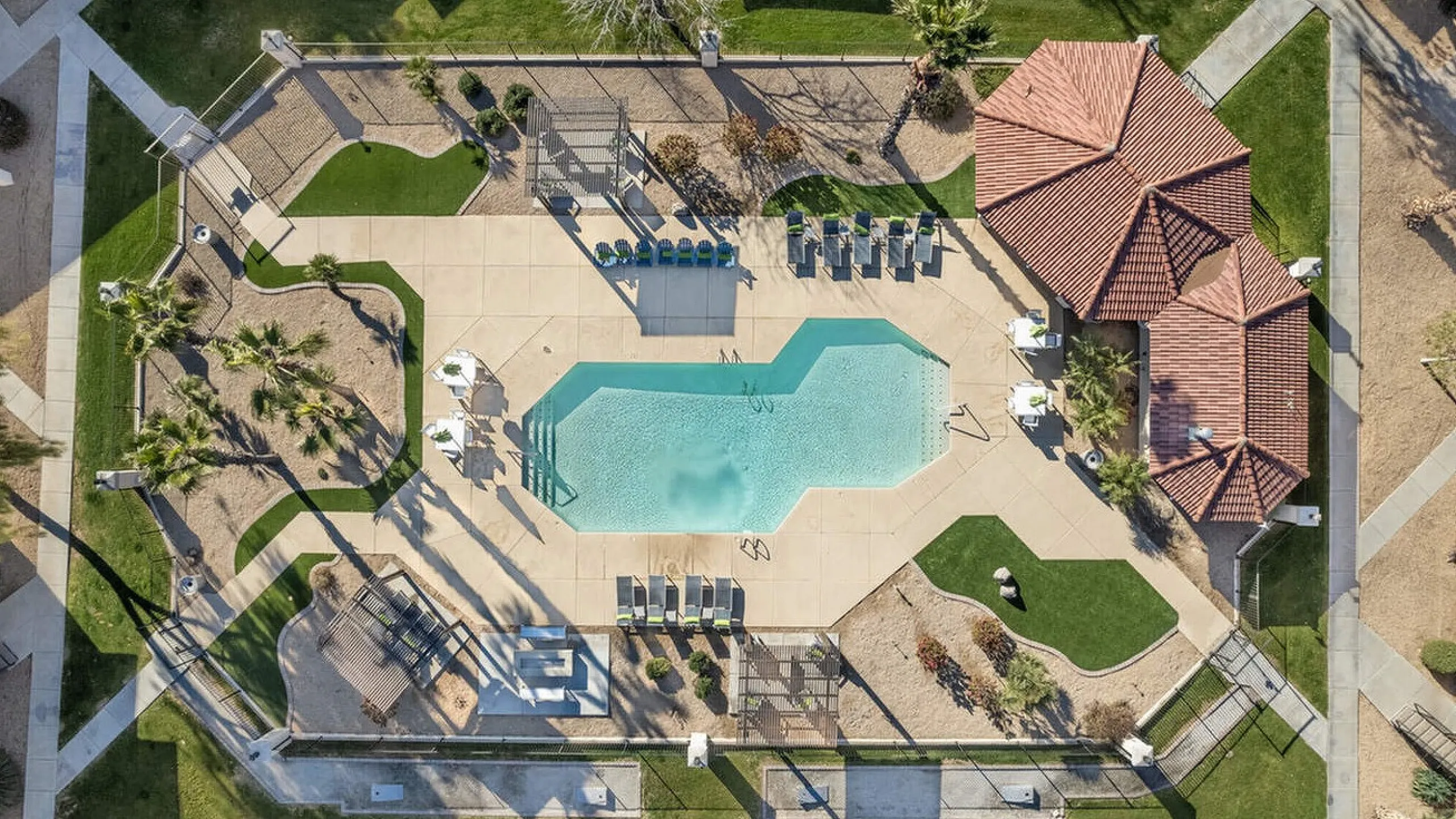 Aerial view of a luxurious outdoor pool area with modern sun loungers, shaded seating, and lush green landscaping, offering a perfect oasis for relaxation and leisure.