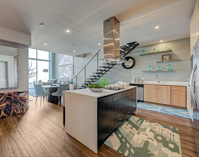 Modern apartment interior featuring an open kitchen with sleek cabinetry, a stylish dining area, and a chic staircase. Bright and airy with natural light accentuating the contemporary decor.