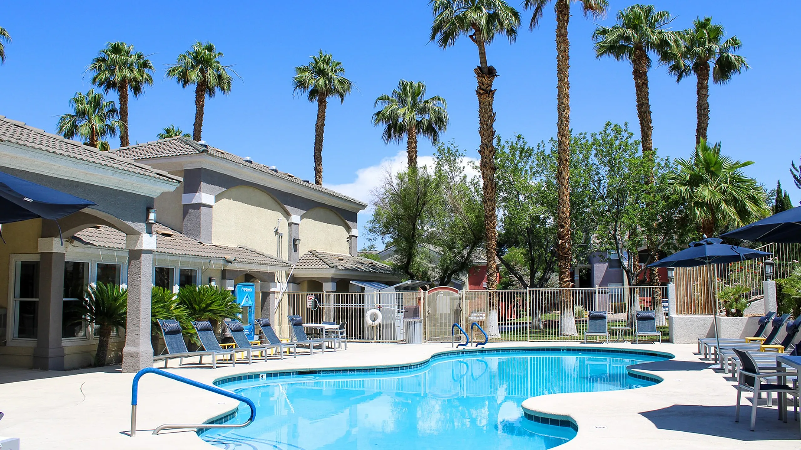 Inviting outdoor swimming pool area with palm trees, sun loungers, and vibrant blue skies, perfect for relaxation and leisure.