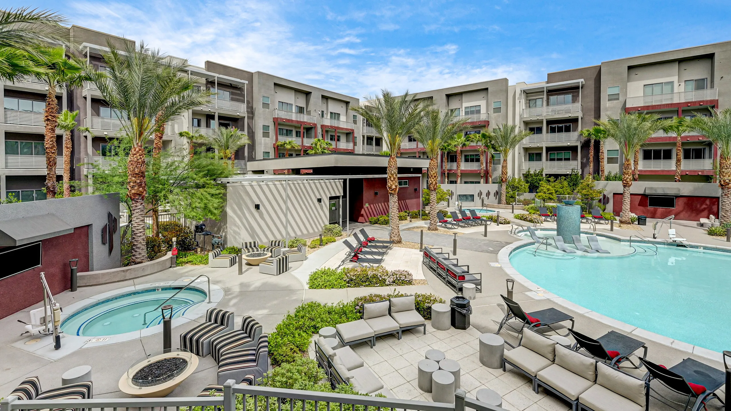 Luxurious apartment complex with a stylish outdoor pool, palm trees, cozy seating areas, and modern architecture under a clear blue sky.