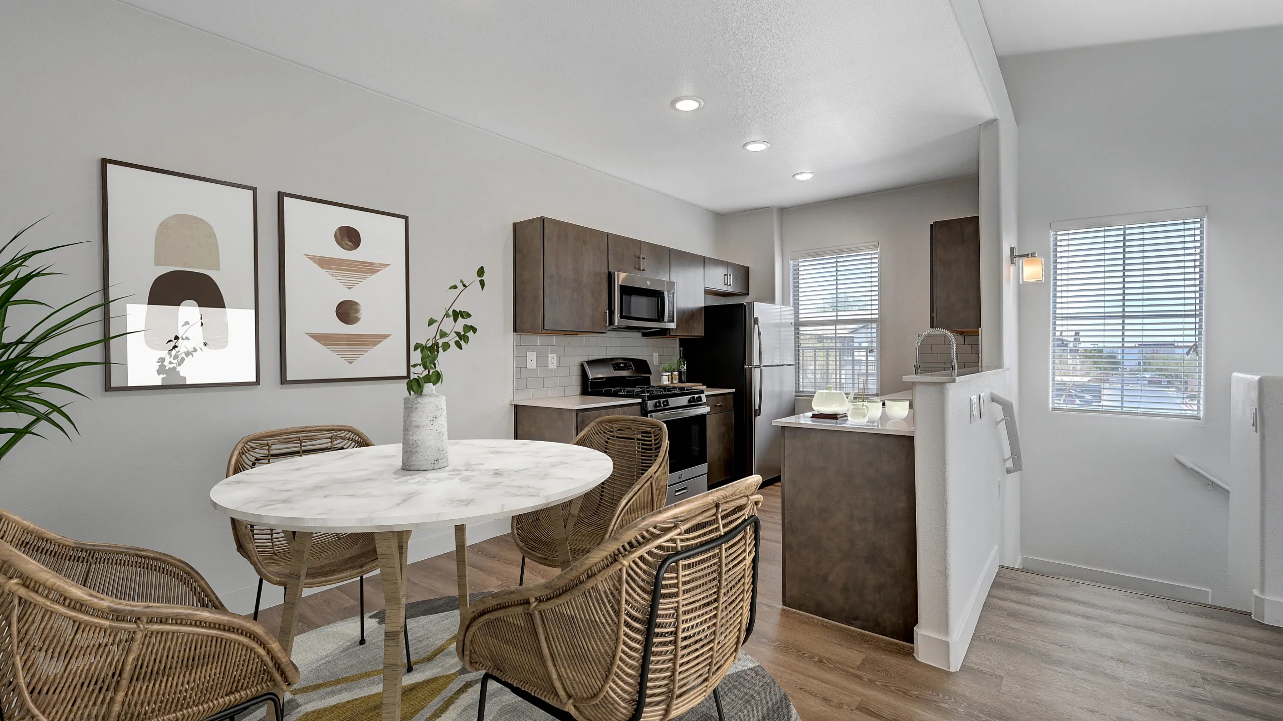 Modern apartment kitchen and dining area featuring a sleek marble table with wicker chairs, contemporary art, and stylish cabinetry.