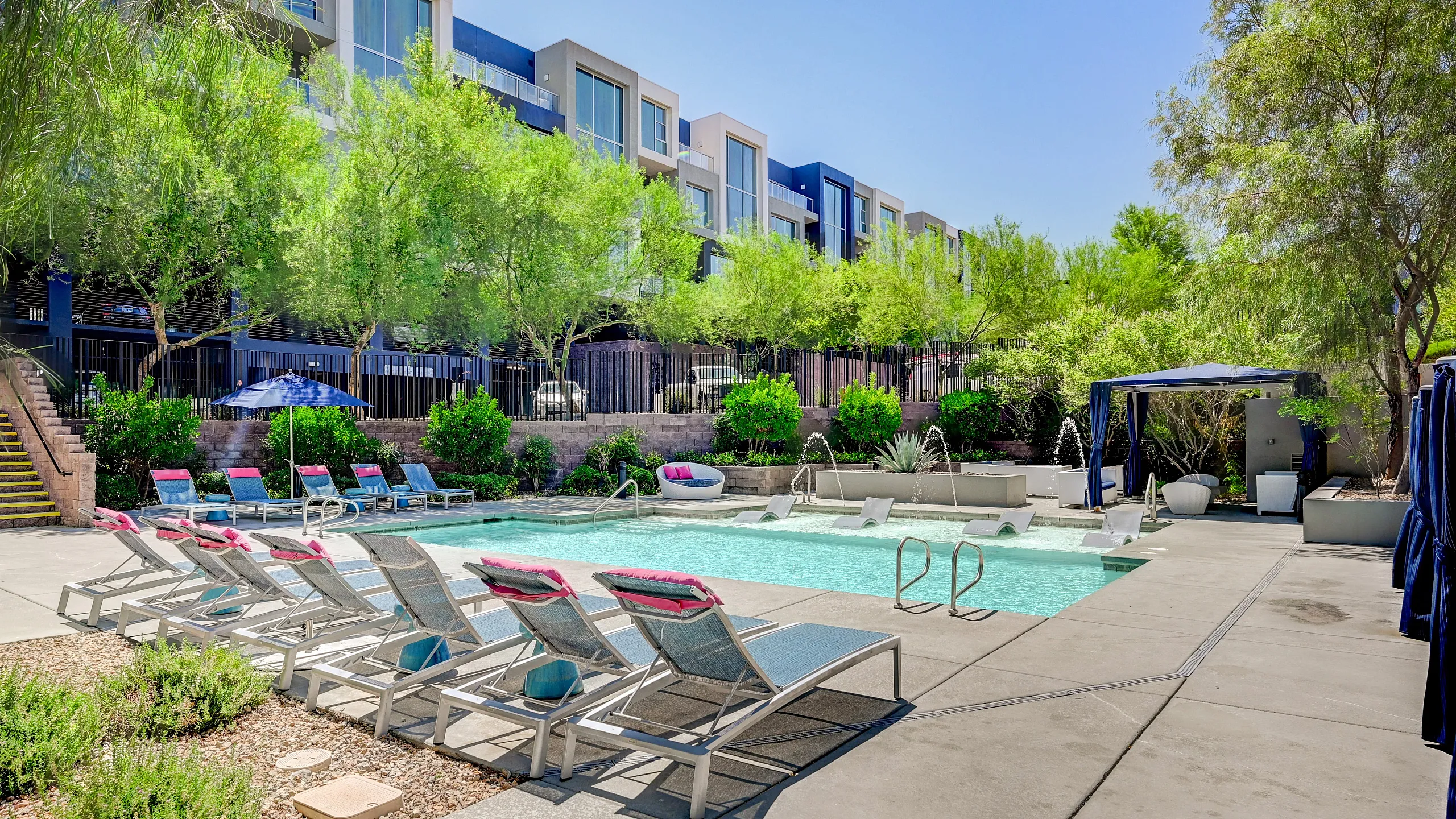 Modern apartment complex with inviting swimming pool, stylish lounge chairs, and lush greenery, perfect for relaxation and leisure.