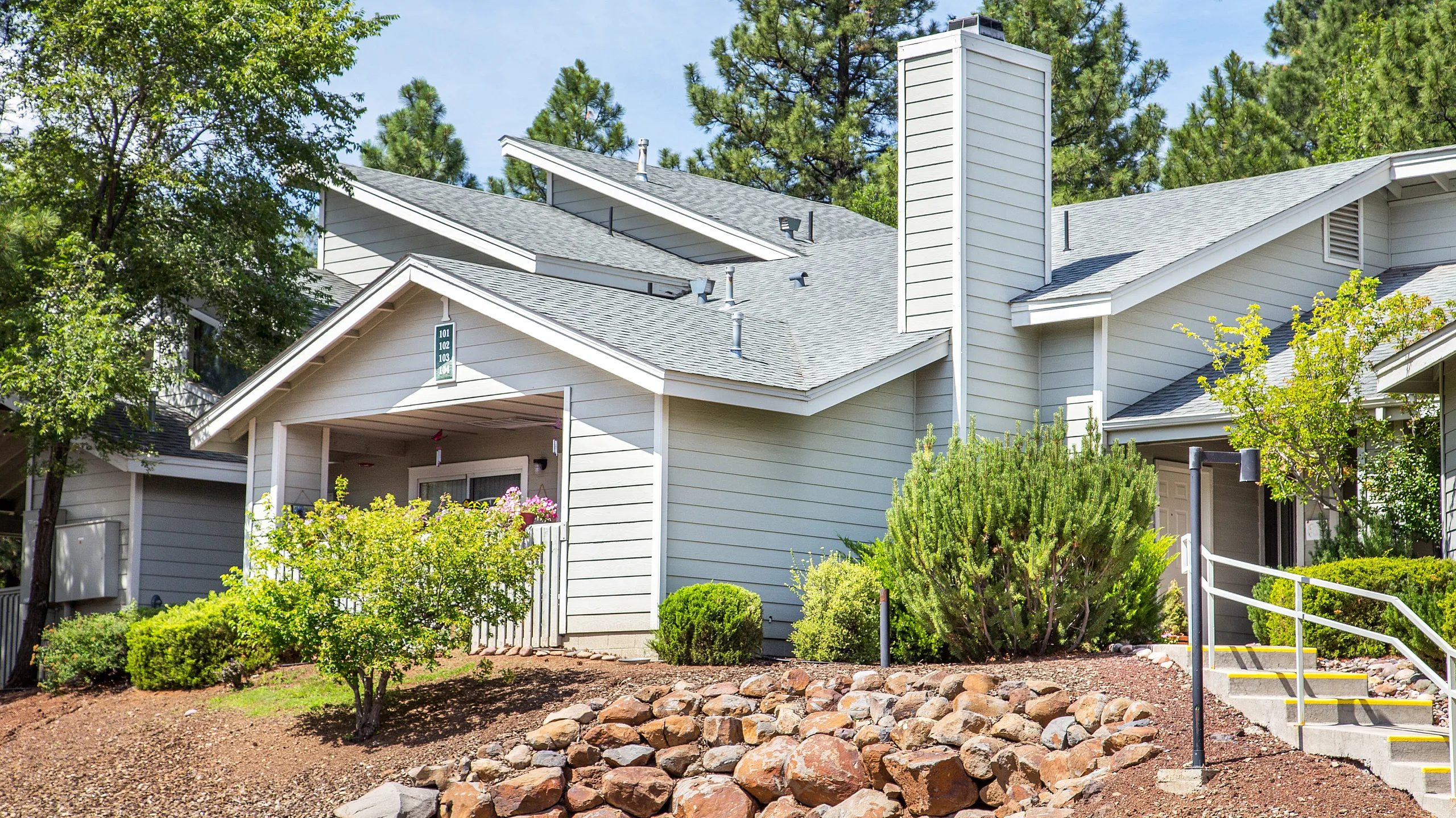 Charming modern house with a cozy porch, surrounded by lush greenery and natural rock landscaping.