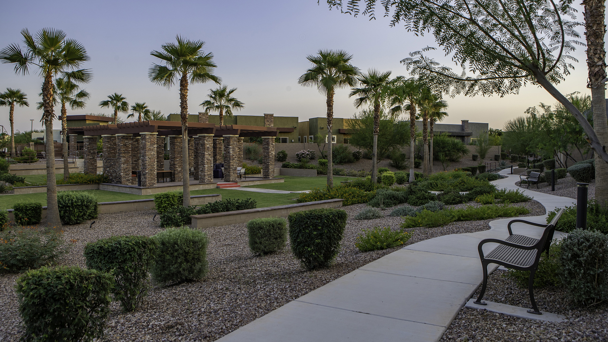 Tranquil outdoor setting with palm trees, stone pergolas, and lush landscaping in a modern apartment complex.