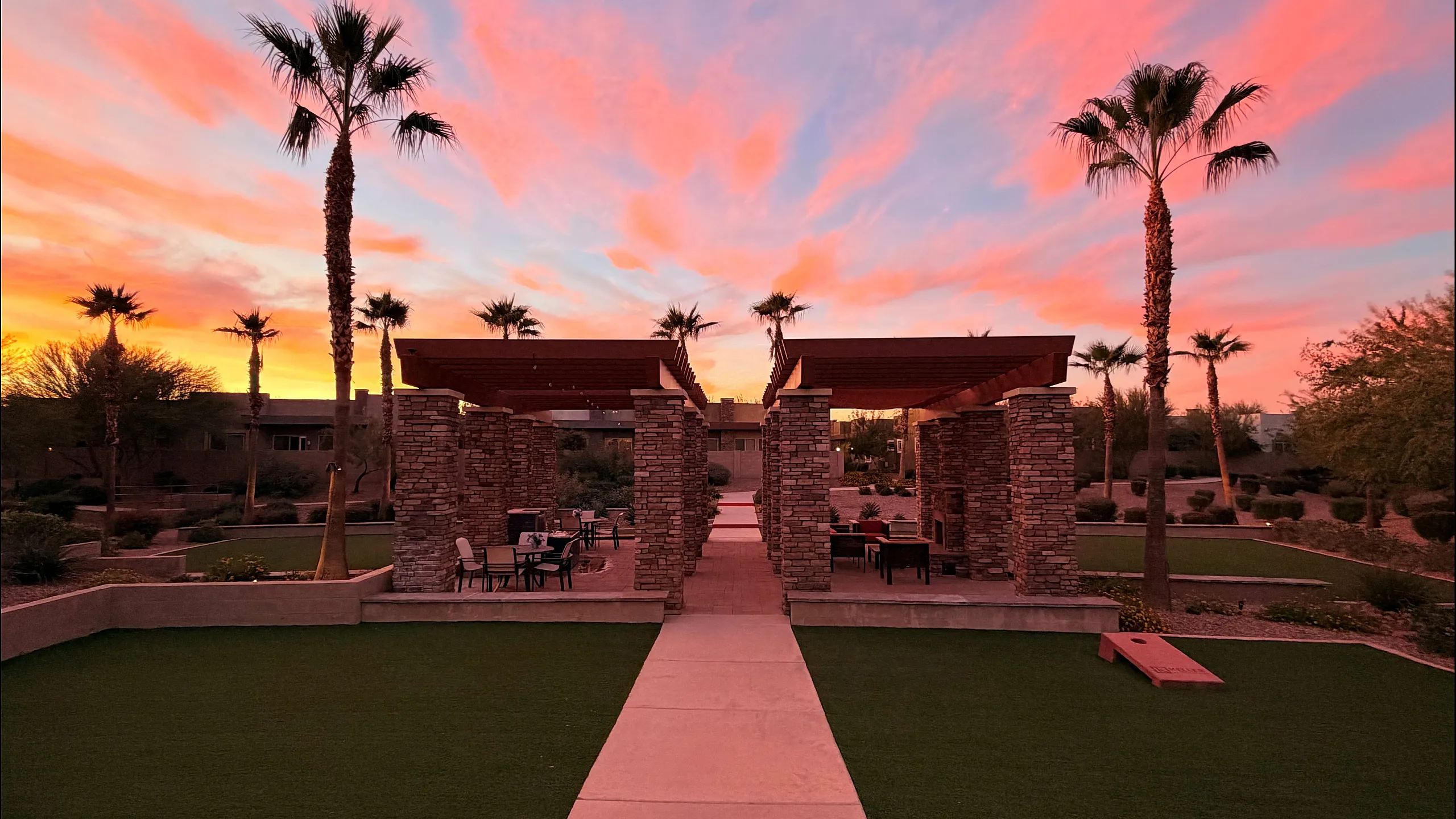 Vibrant outdoor living space with palm trees and pergolas under a stunning sunset sky.